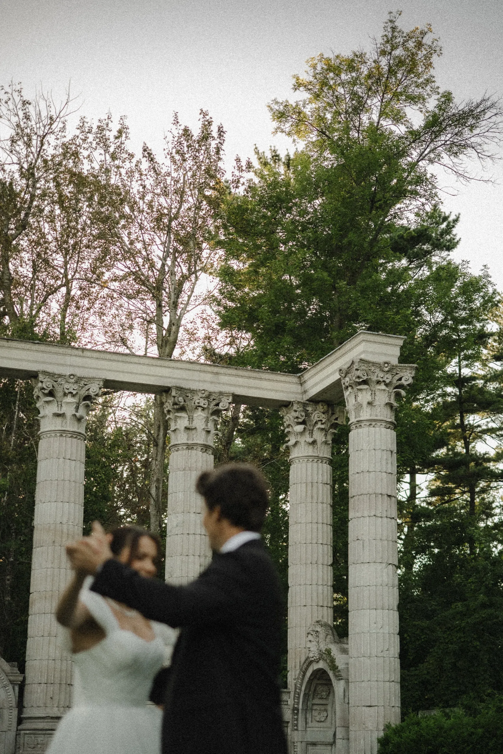 Low angle of the tall fluted columns at Guild Park, with the bride and groom dancing small at their base, by AD Photography