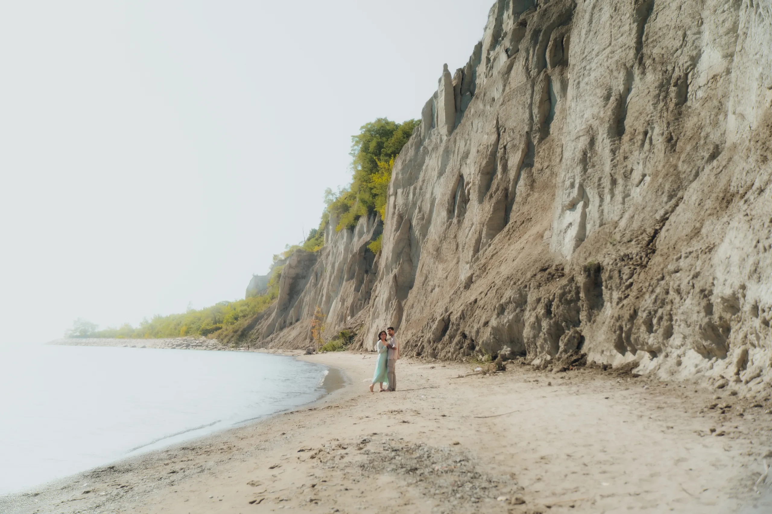 Swati and Saksham embrace at the base of the towering Scarborough Bluffs on the beach, by AD Photography