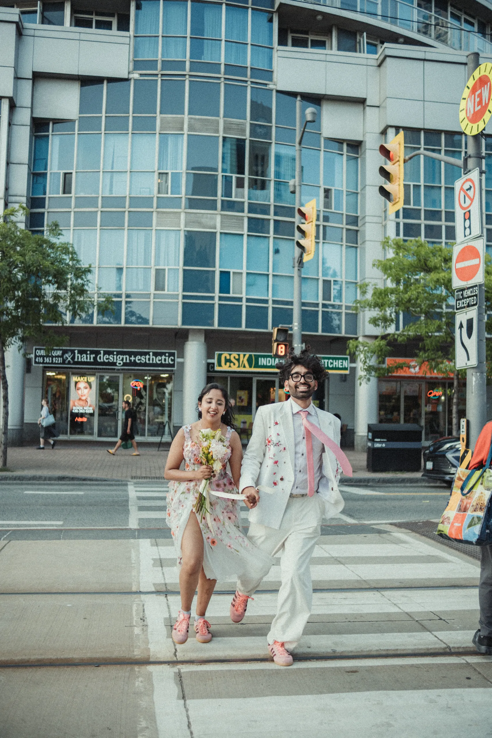 Harsh and Payal crossing a downtown Toronto intersection in coral floral wedding outfits, by AD Photography