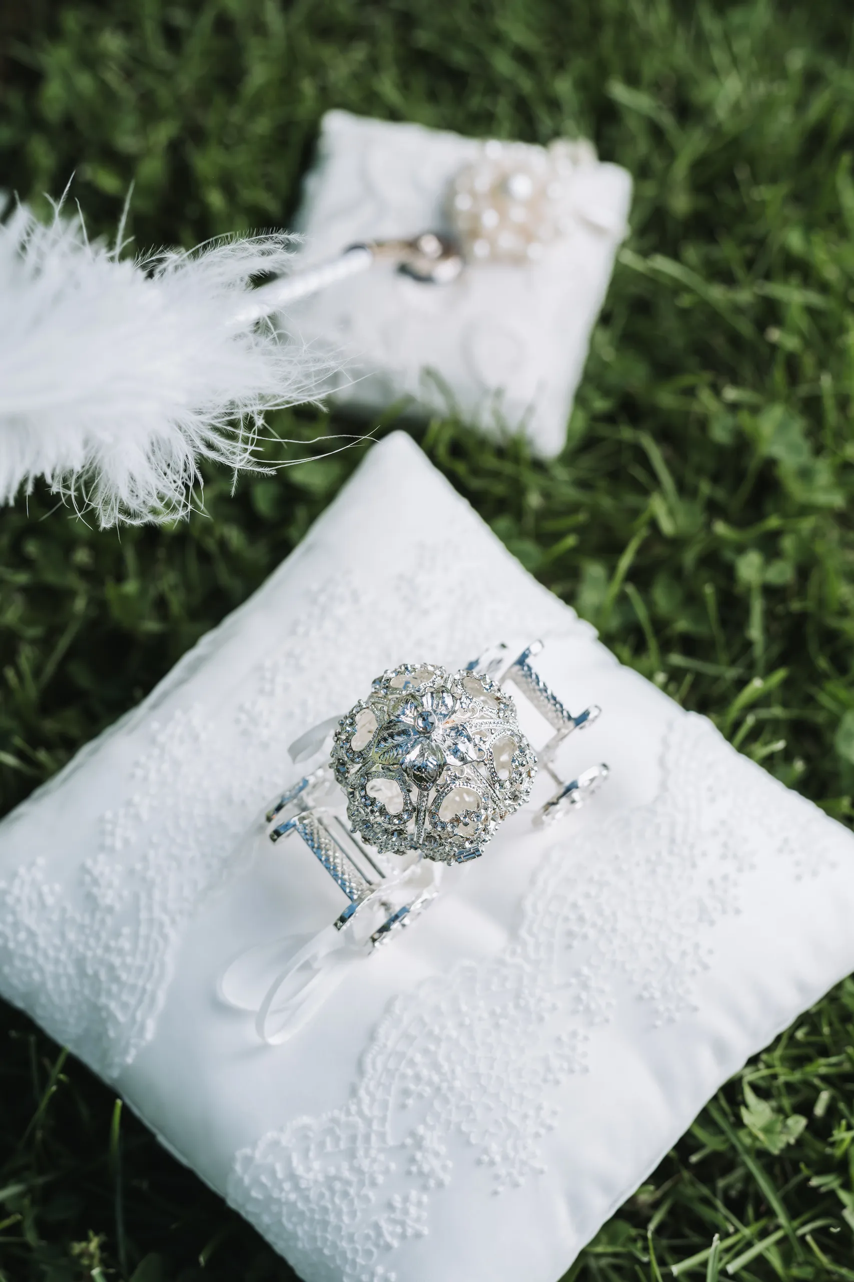 Wedding rings and a white feather quill resting on lace ring pillows in the grass at the Niagara Parks Botanical Gardens, by AD Photography