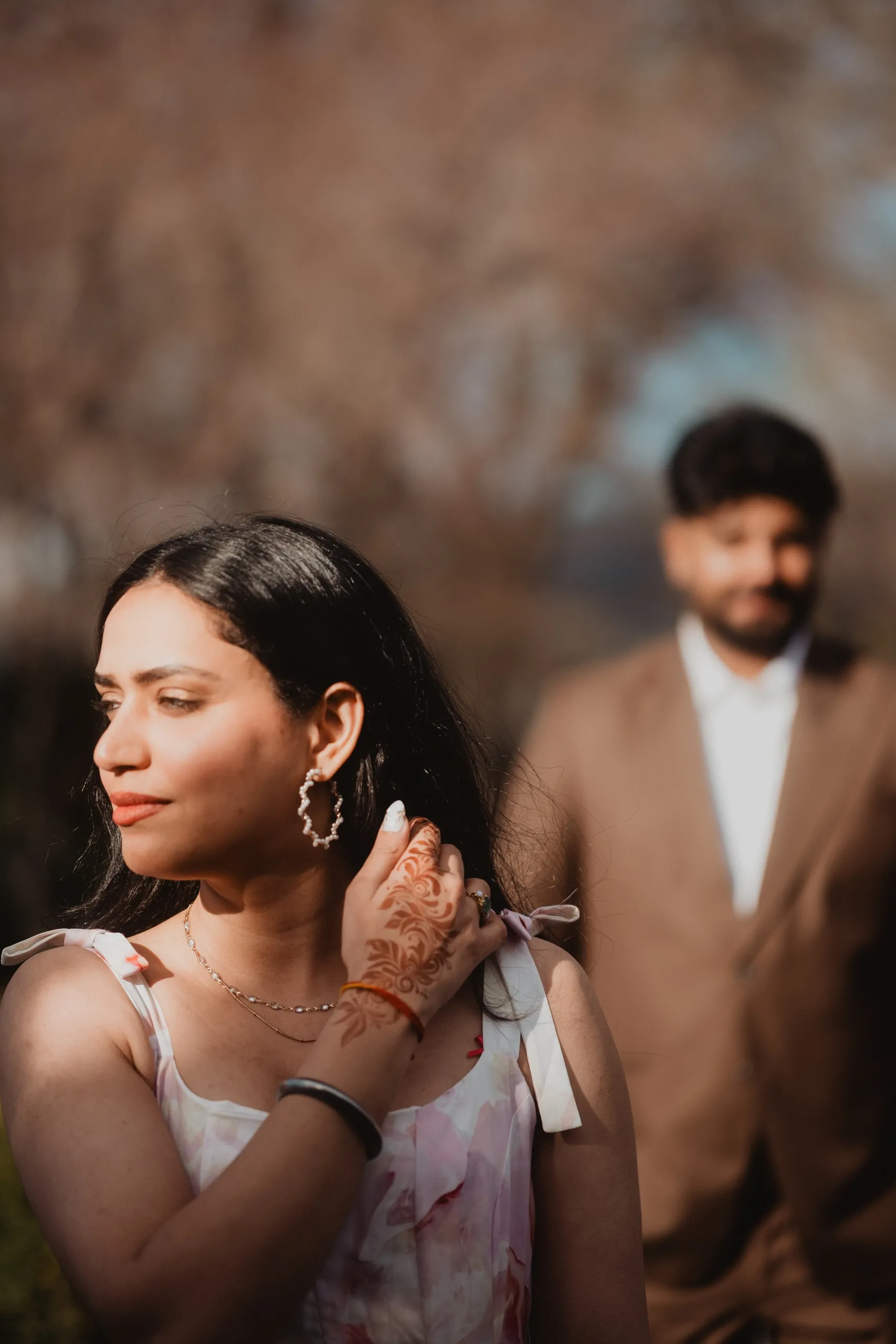 Mehak in focus with henna running across her hand while Kamal waits blurred behind, by AD Photography