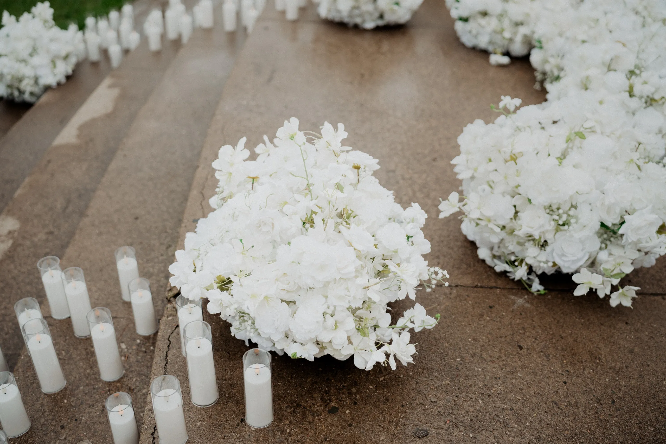 White floral clusters and glass pillar candles lining the wet stone steps of the colonnade, by AD Photography