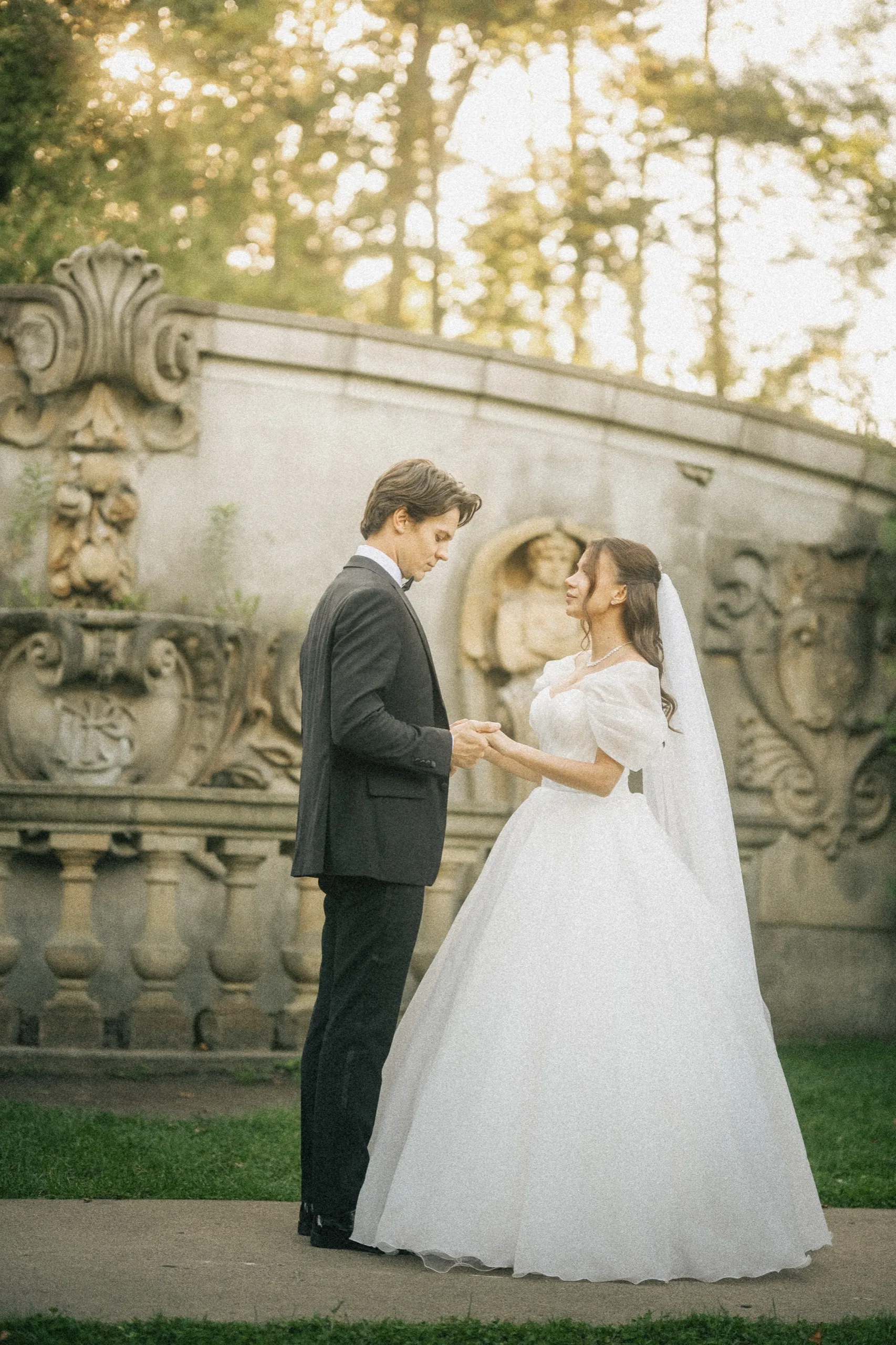 Bride and groom holding hands in front of the curved carved stone wall at Guild Park & Gardens, by AD Photography