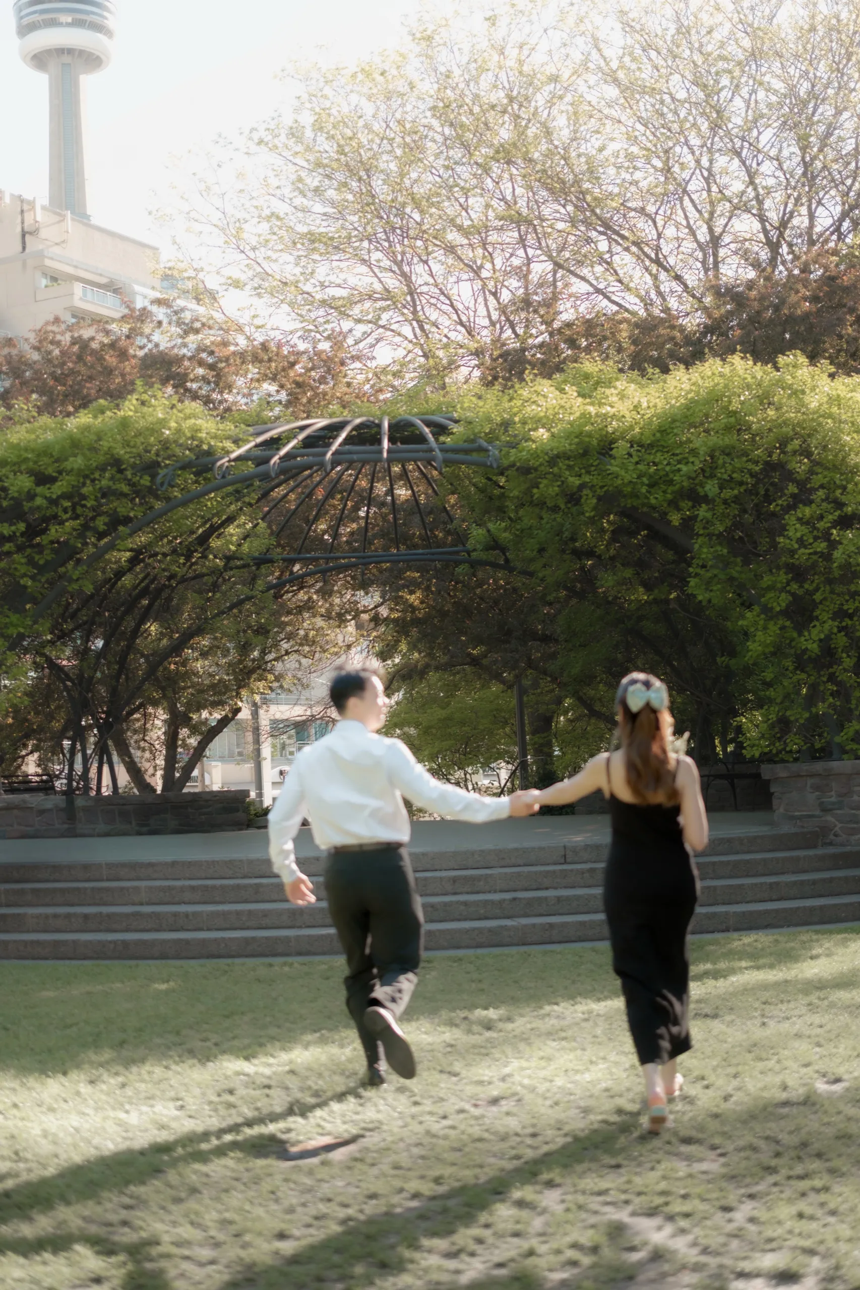 Nelson leaps into the air in front of the spring blossoms while Josie laughs, downtown Toronto skyline beyond, by AD Photography