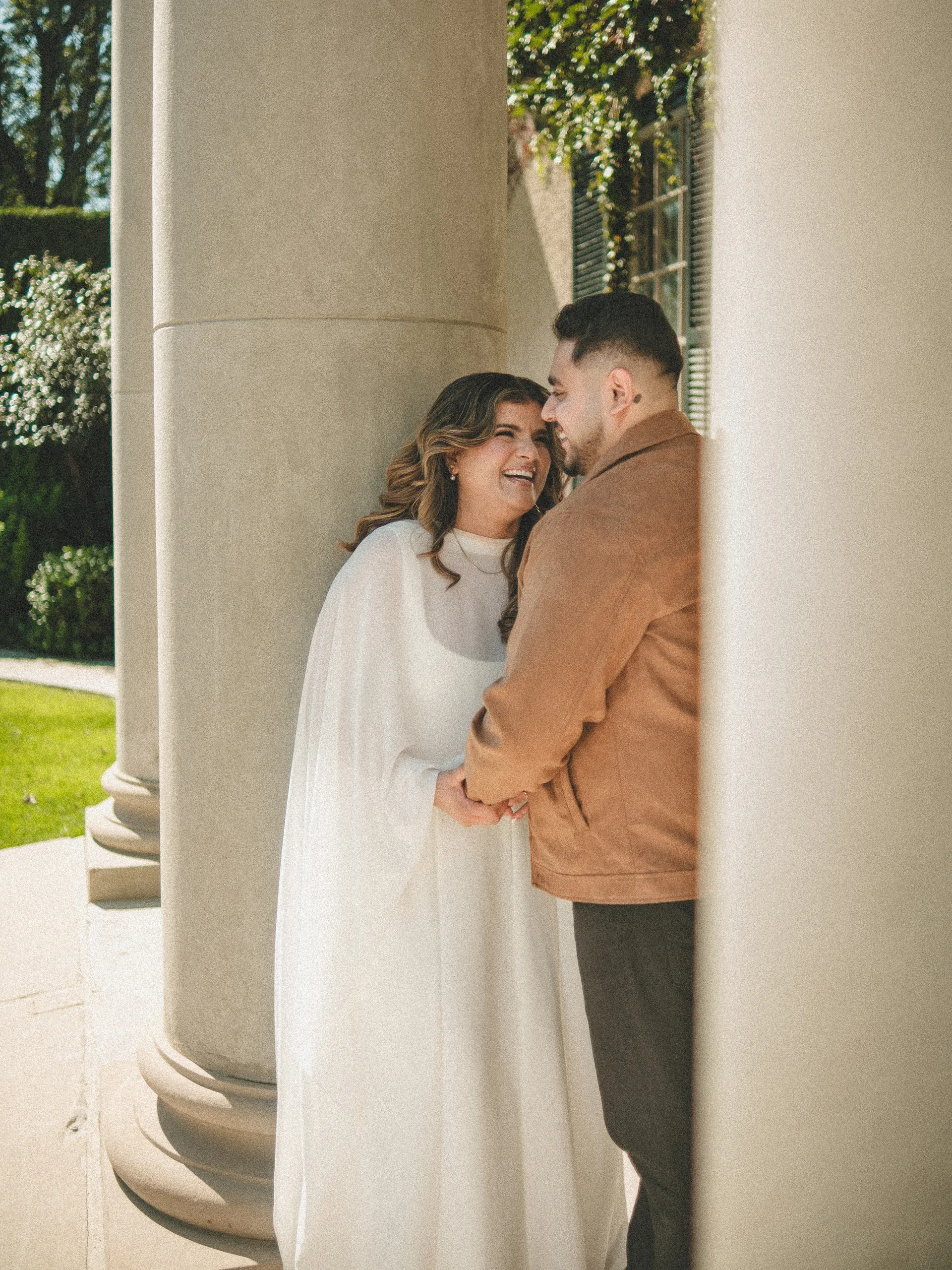 Parneet laughing as Maninder leans in close between stone columns at Parkwood Estate in Oshawa, by AD Photography