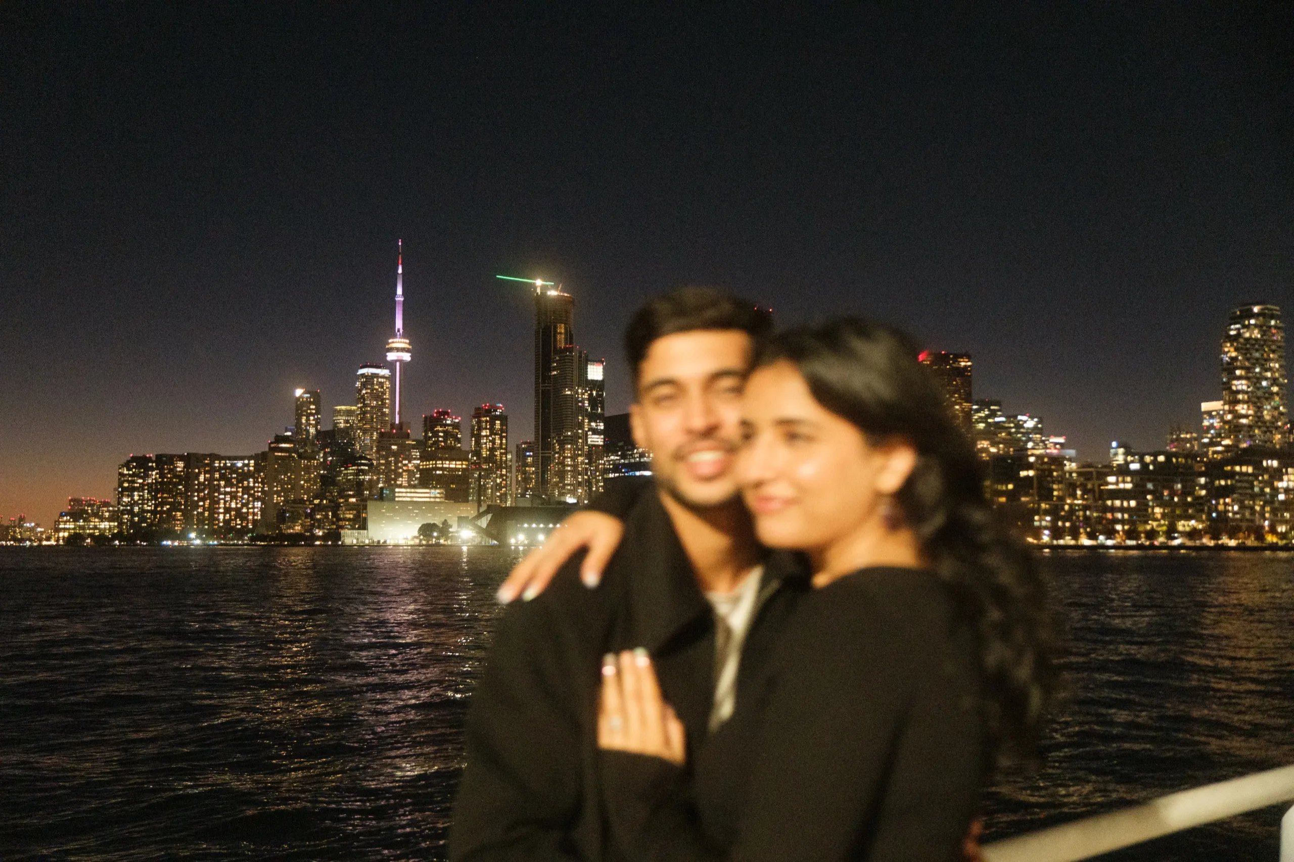 Focus falls on the lit Toronto skyline while Swati and Saksham blur softly in front, by AD Photography