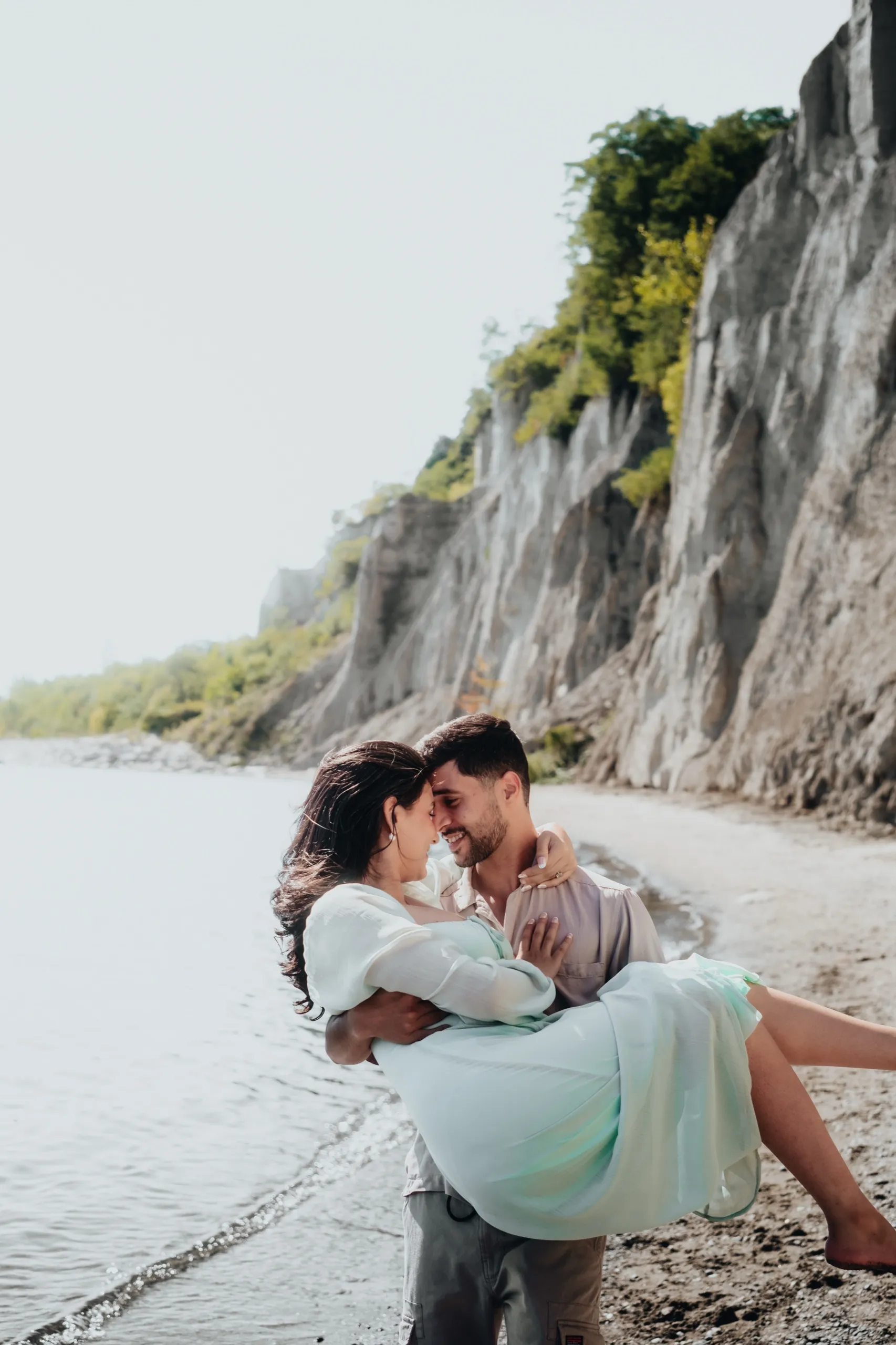 Saksham carries Swati along the waterline, foreheads touching, below the white cliffs at Bluffs Beach, by AD Photography