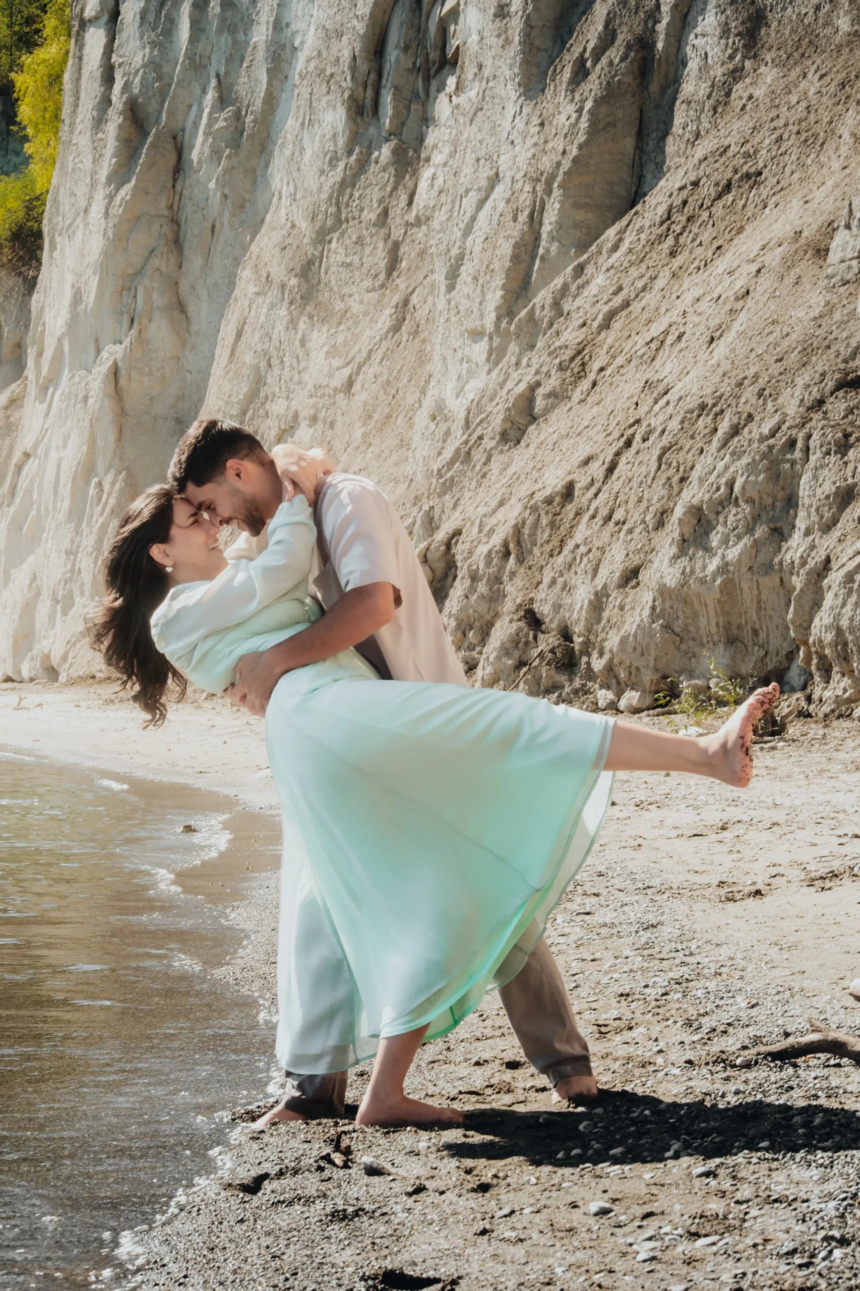 A couple dips at the waterline below the white cliffs at Bluffers Park beach, mint dress fanned, by AD Photography