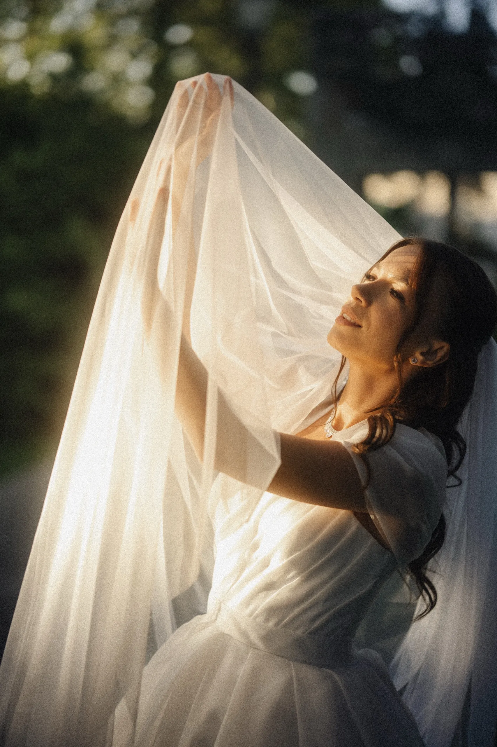 Bride in profile lifting her veil to the low evening sun at Guild Park, the tulle glowing gold, by AD Photography