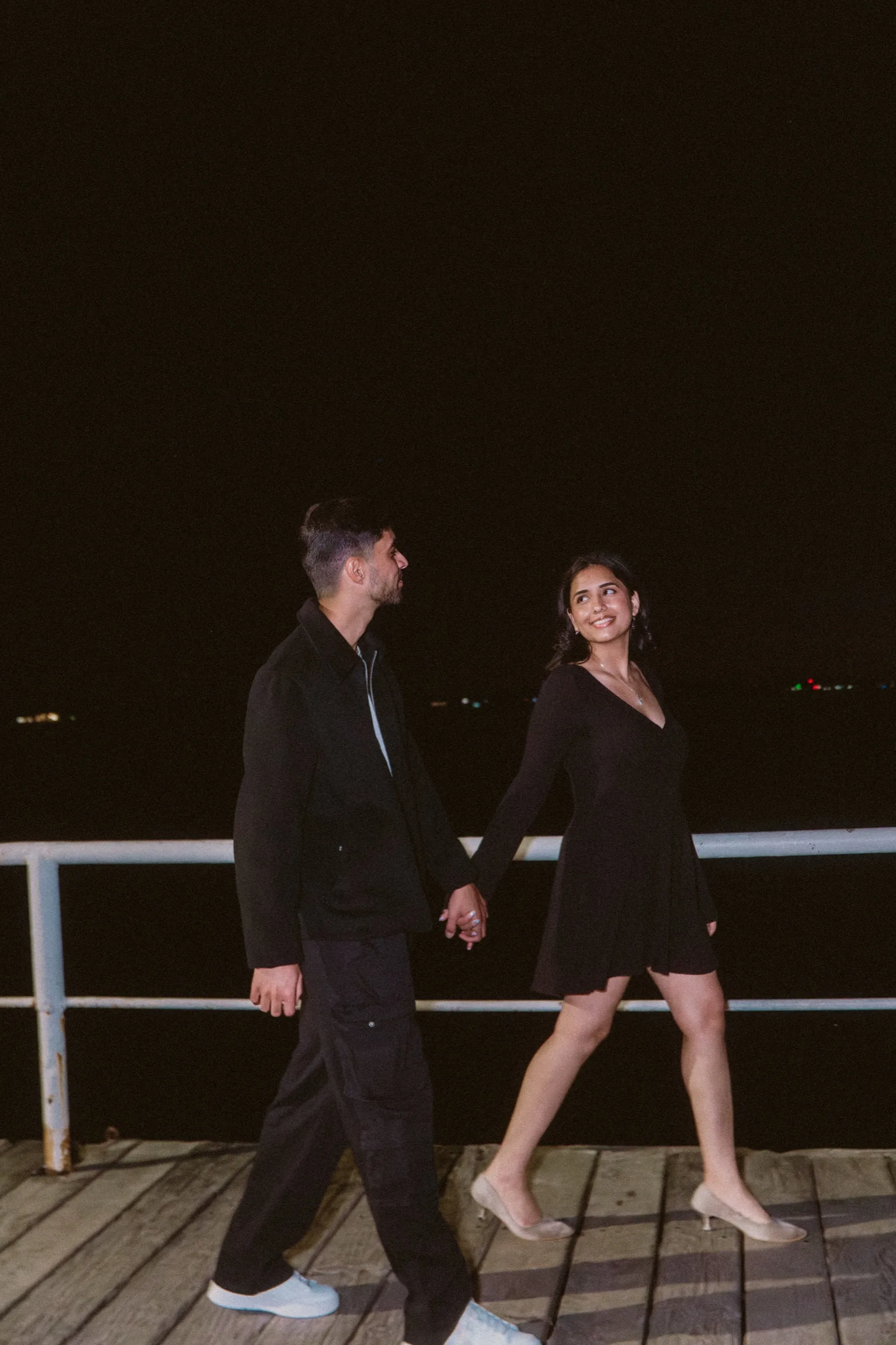 Swati strides the dark boardwalk in kitten heels, leading Saksham by the hand, by AD Photography