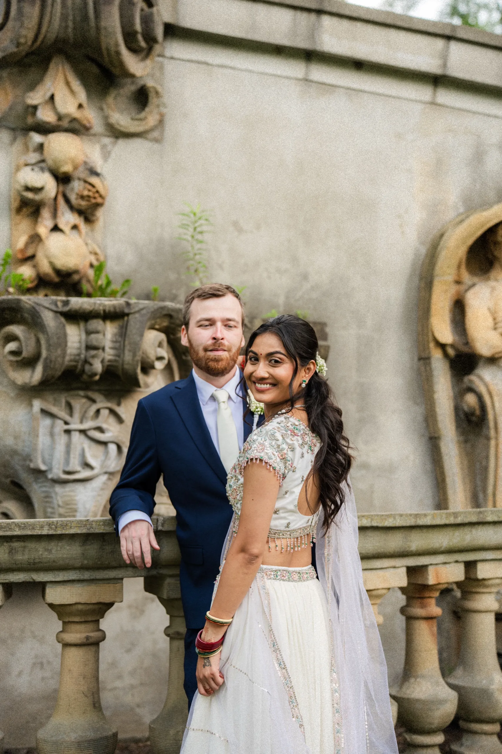 Nidhi glances back with a smile as Derek stays close on the old stone balustrade., by AD Photography