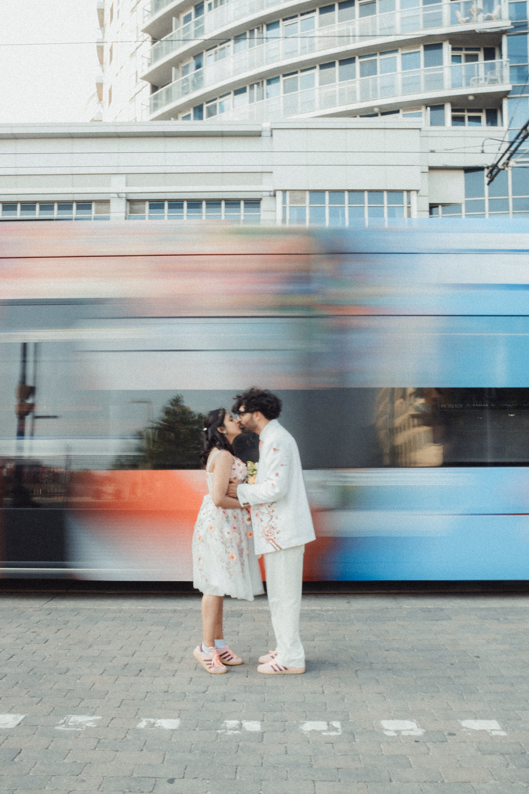 A couple kissing perfectly still as a Toronto streetcar blurs past behind them, by AD Photography