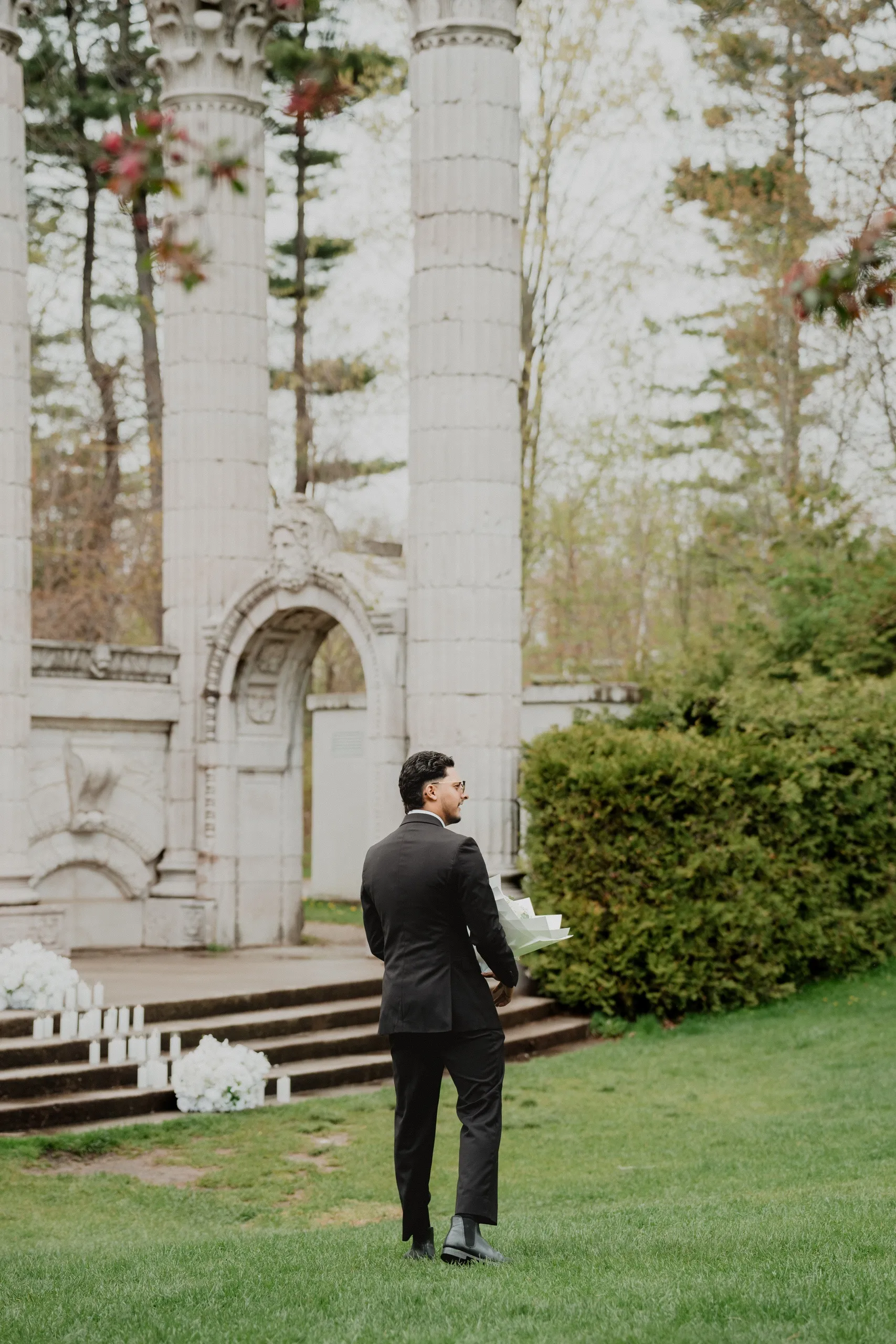 Raeed crossing the lawn toward the Greek theatre colonnade with a wrapped bouquet held at his side, by AD Photography