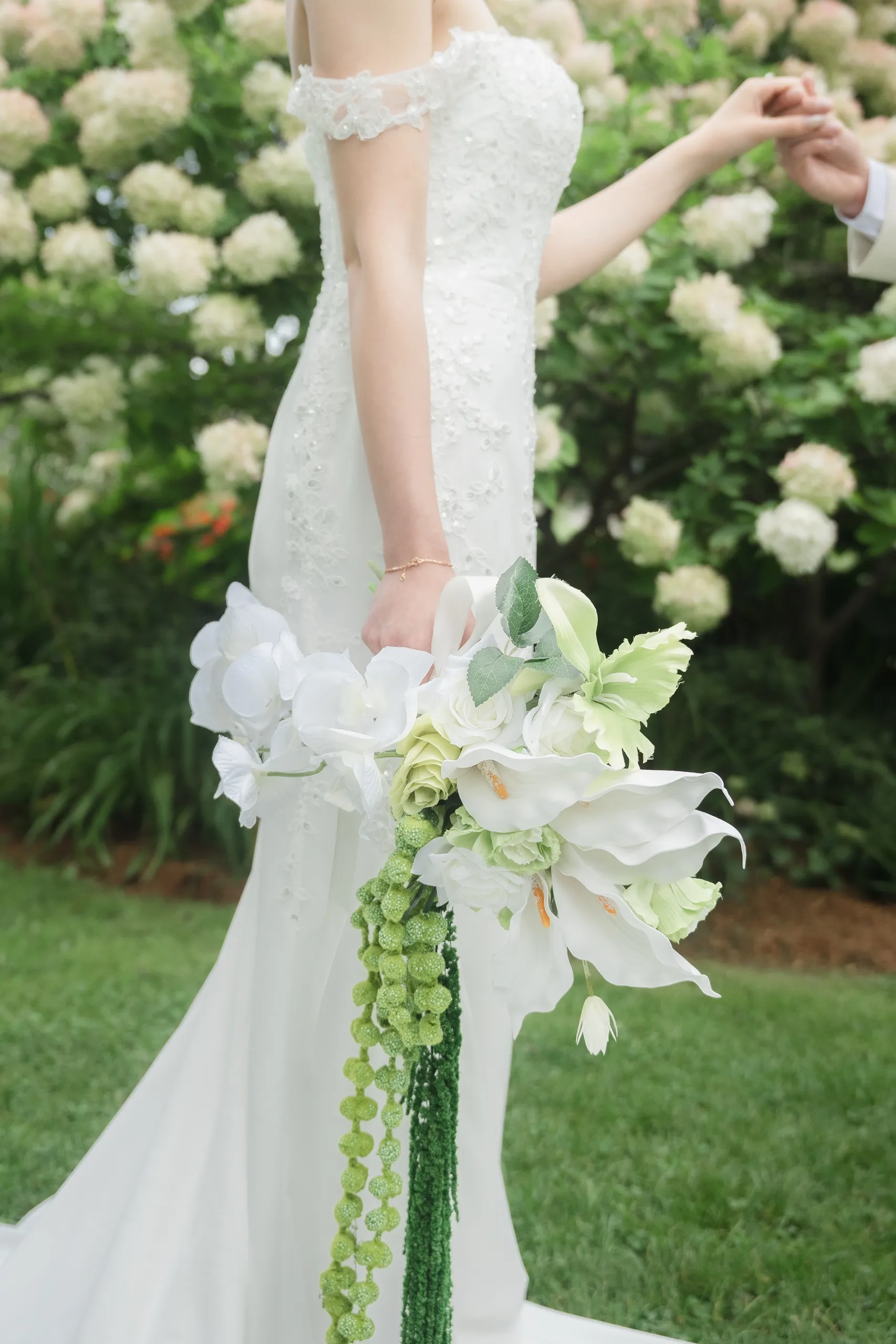 Josie's cascading white orchid bouquet and lace gown, her hand reaching for Nelson's, by AD Photography