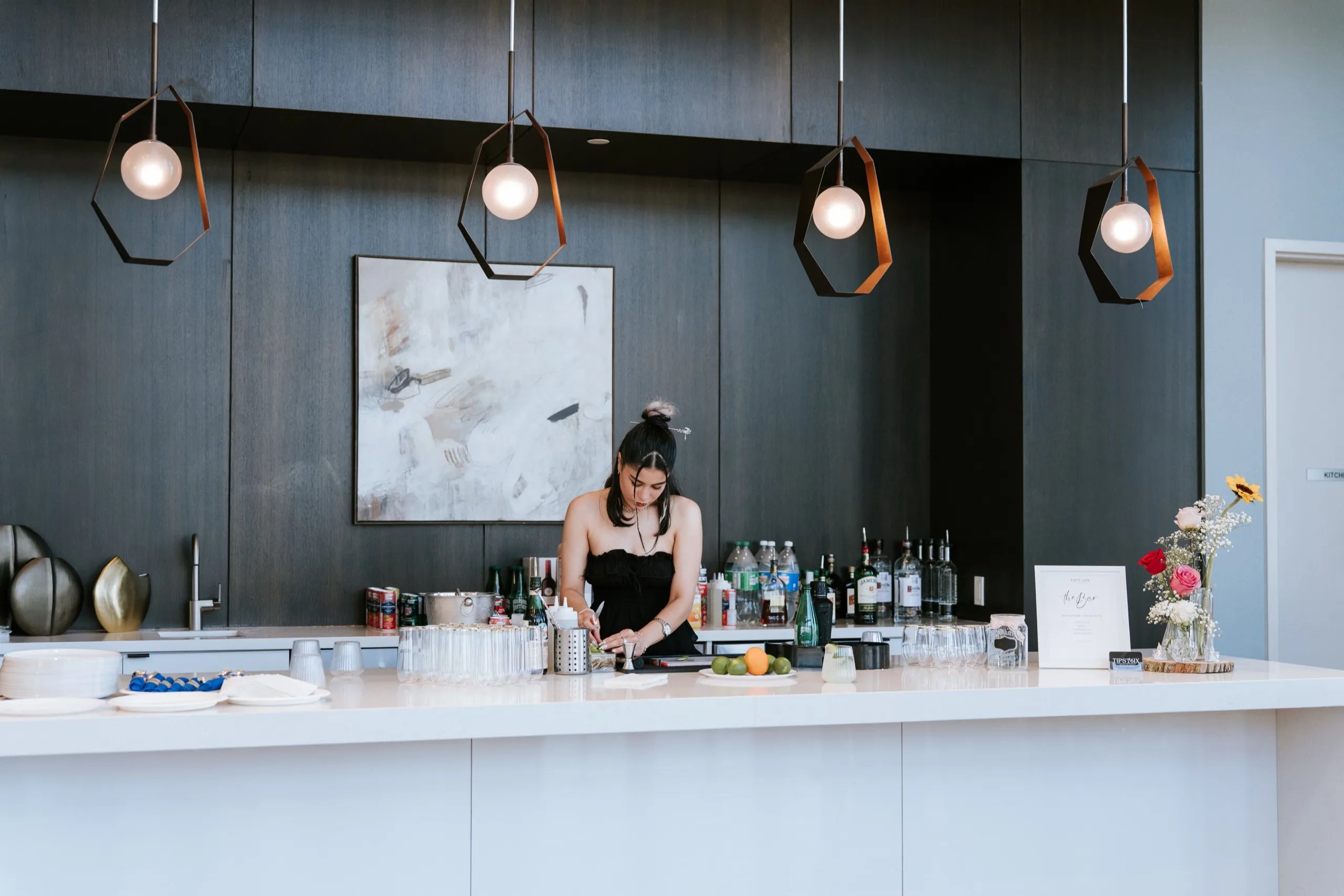 The bartender sets up under pendant lights at the dark wood bar before guests arrive, by AD Photography