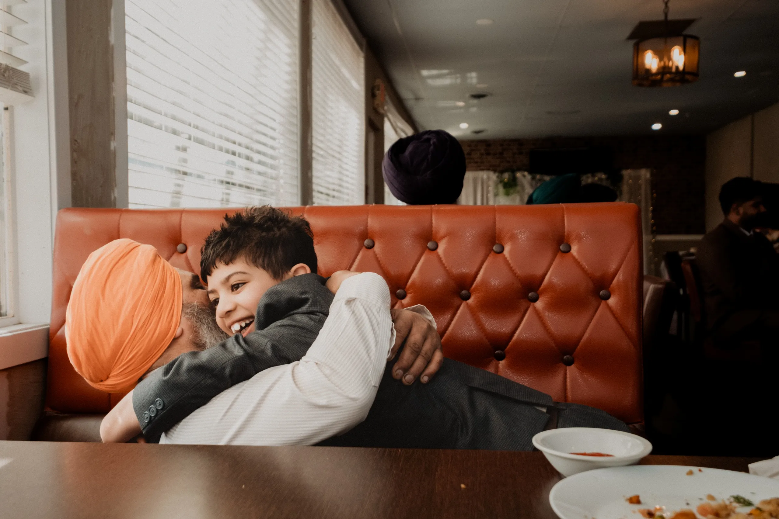 A young boy hugging his grandfather in a restaurant booth after the civil ceremony, by AD Photography