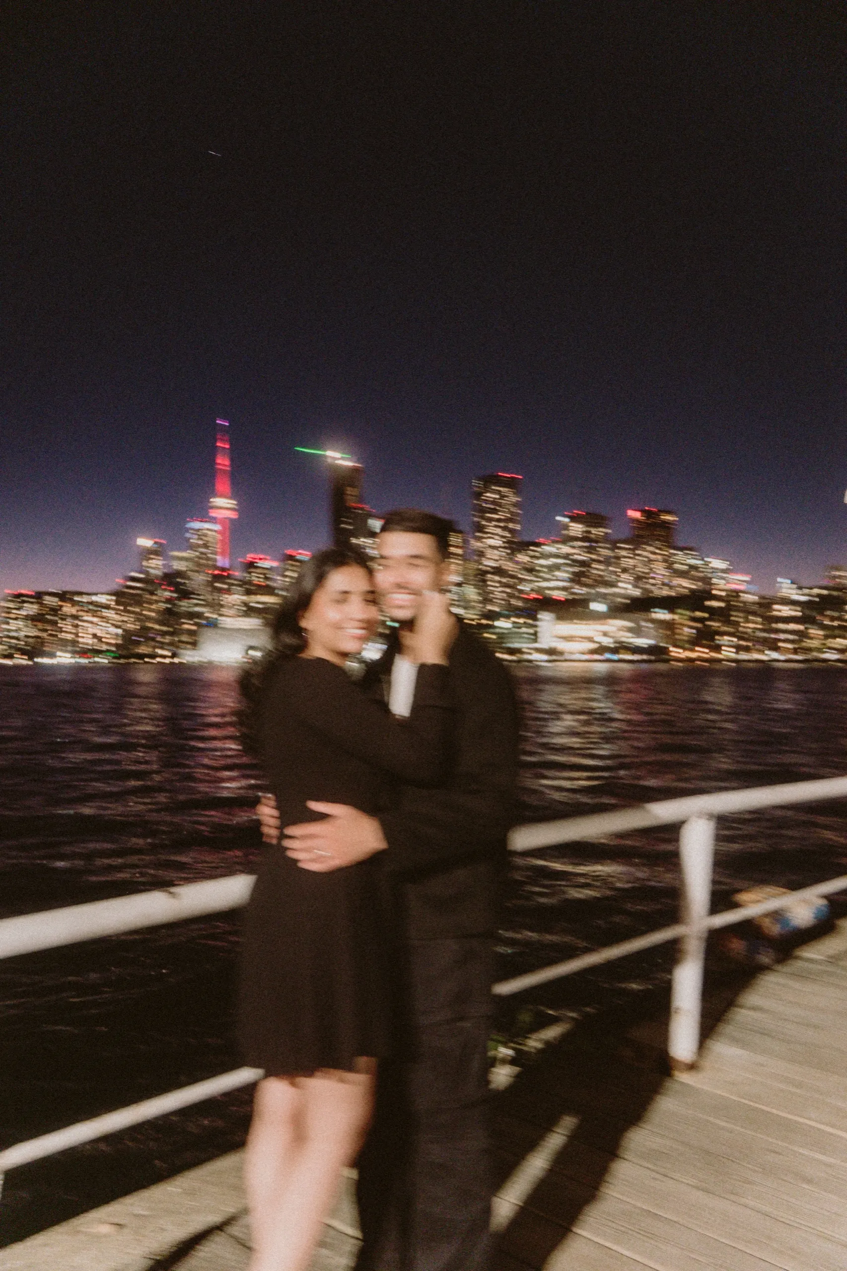 Playful motion blur hug on the boardwalk, CN Tower glowing red across the harbour, by AD Photography