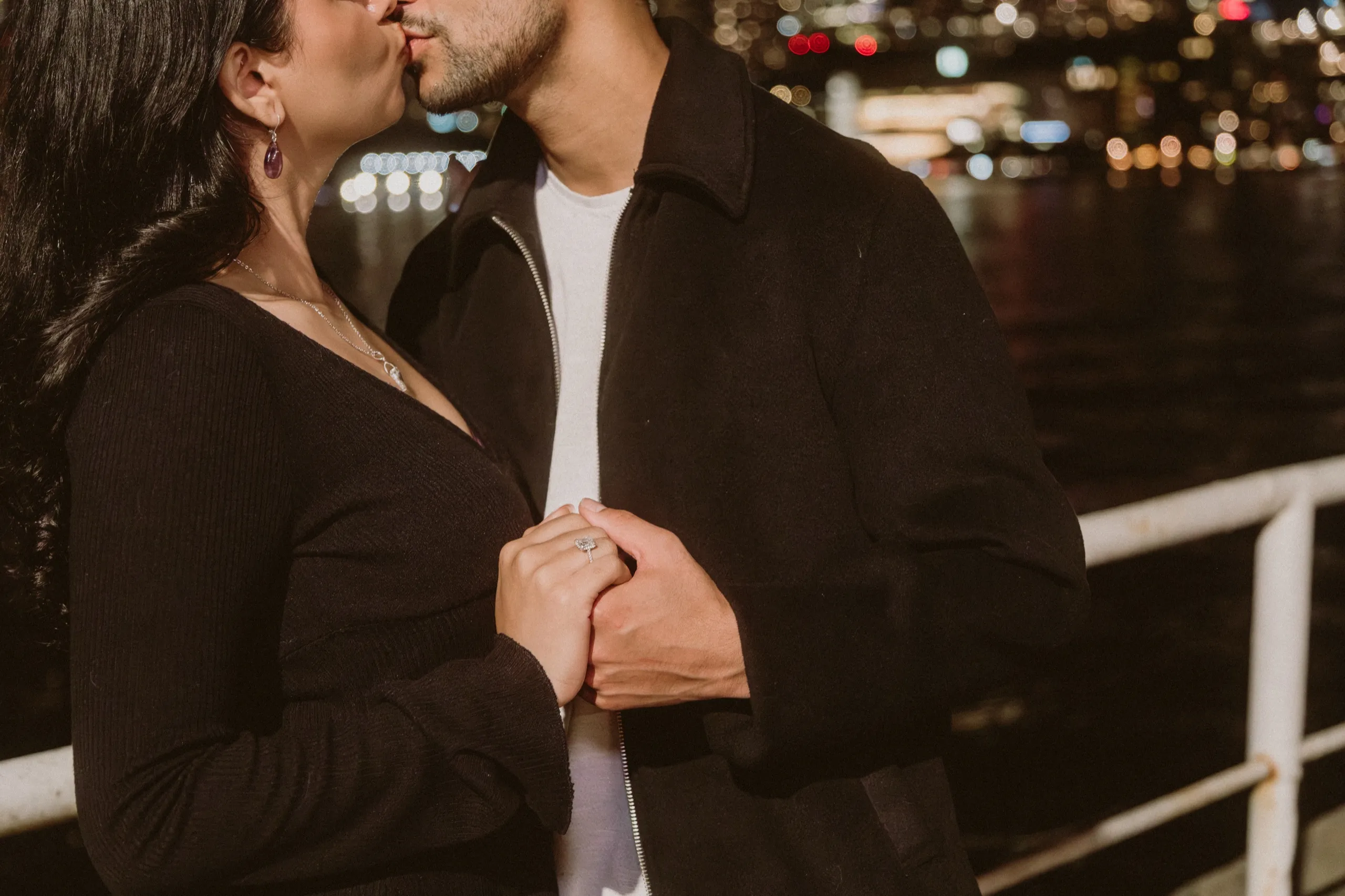 Anonymous crop of a kiss at night, engagement ring centred against the city bokeh, by AD Photography