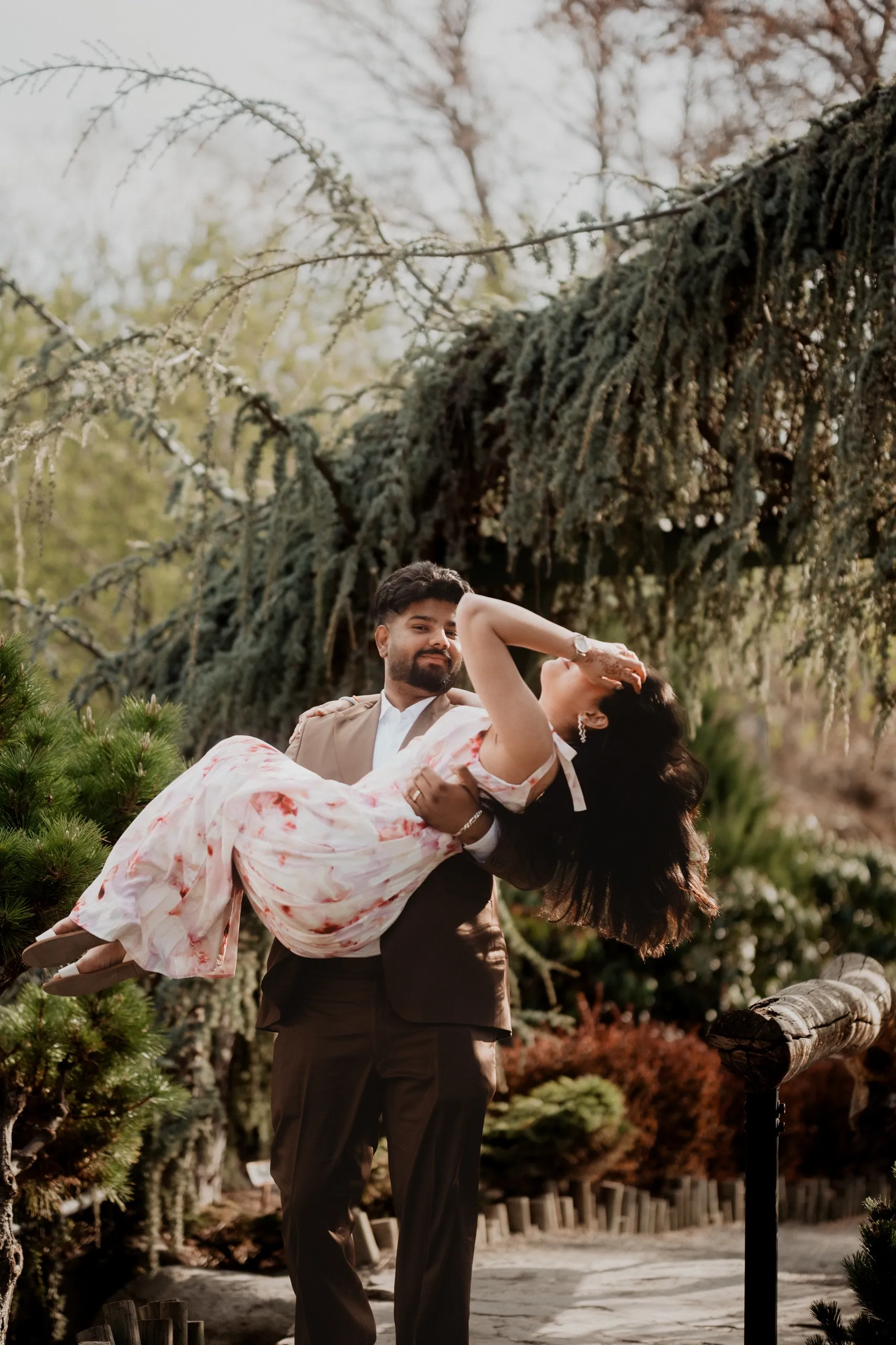 Kamal lifting Mehak off her feet under a wide cedar, her hair falling back, by AD Photography