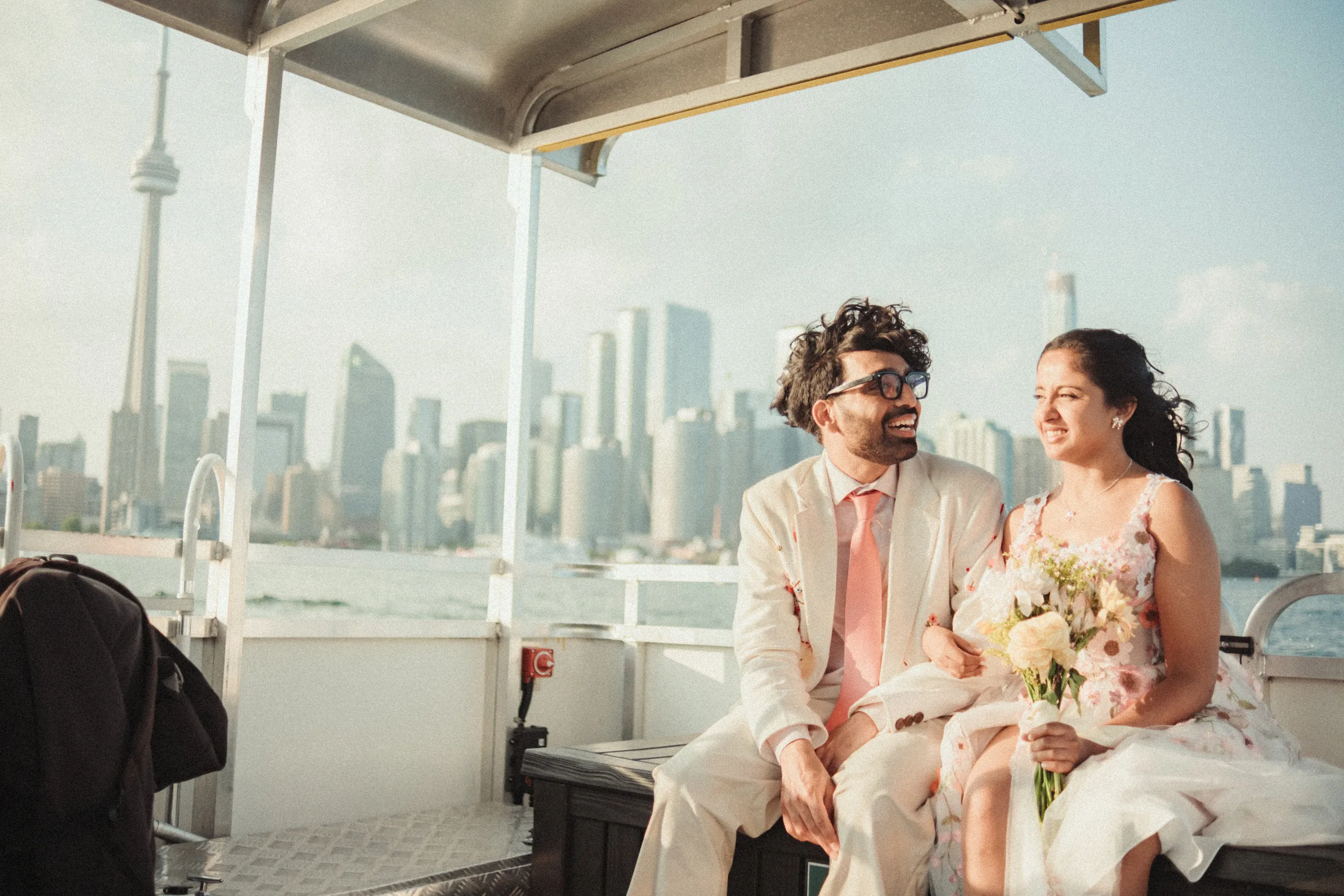 Harsh and Payal on the Toronto Island ferry deck with the CN Tower and downtown skyline behind them, by AD Photography