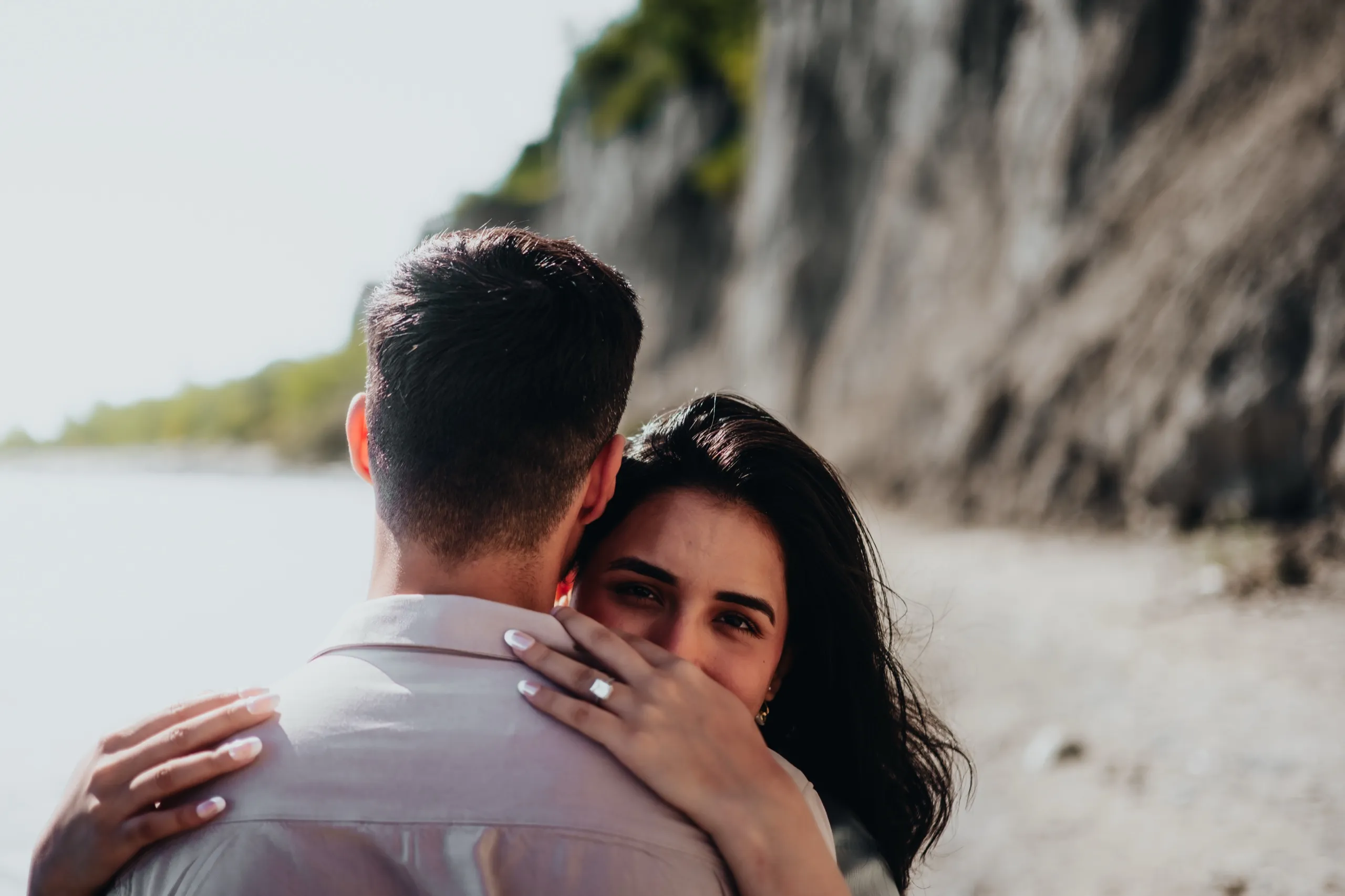 Swati peeks over Saksham's shoulder, engagement ring resting on his neck, cliffs behind, by AD Photography