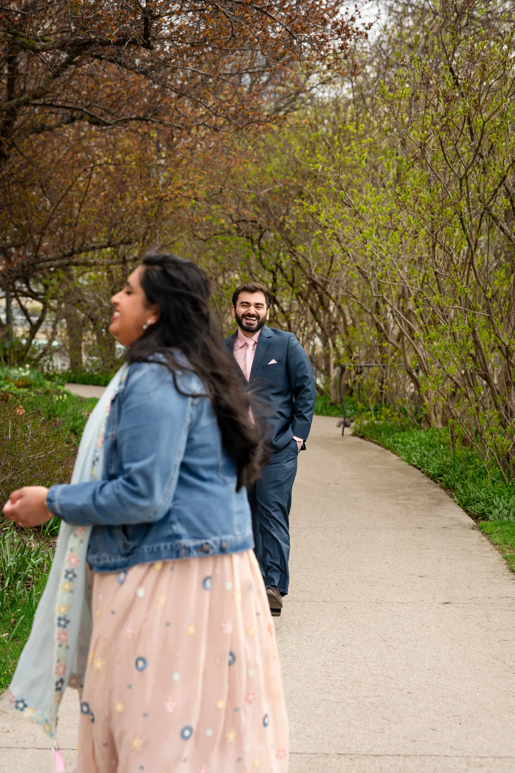 Nadia walks ahead in soft focus as Abdullah follows along a spring garden path in Toronto, by AD Photography