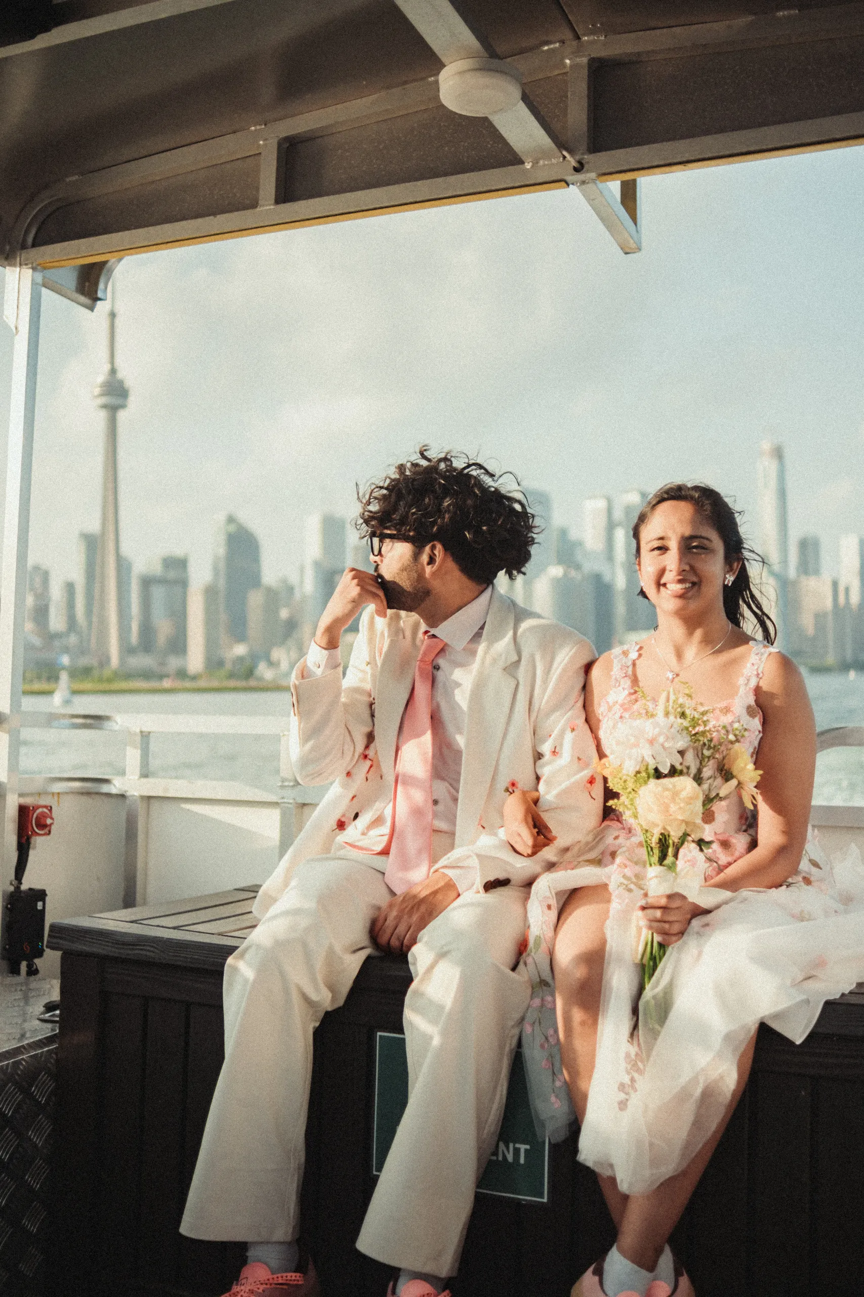 Harsh and Payal seated on the ferry to the Toronto Islands, skyline in the background, by AD Photography