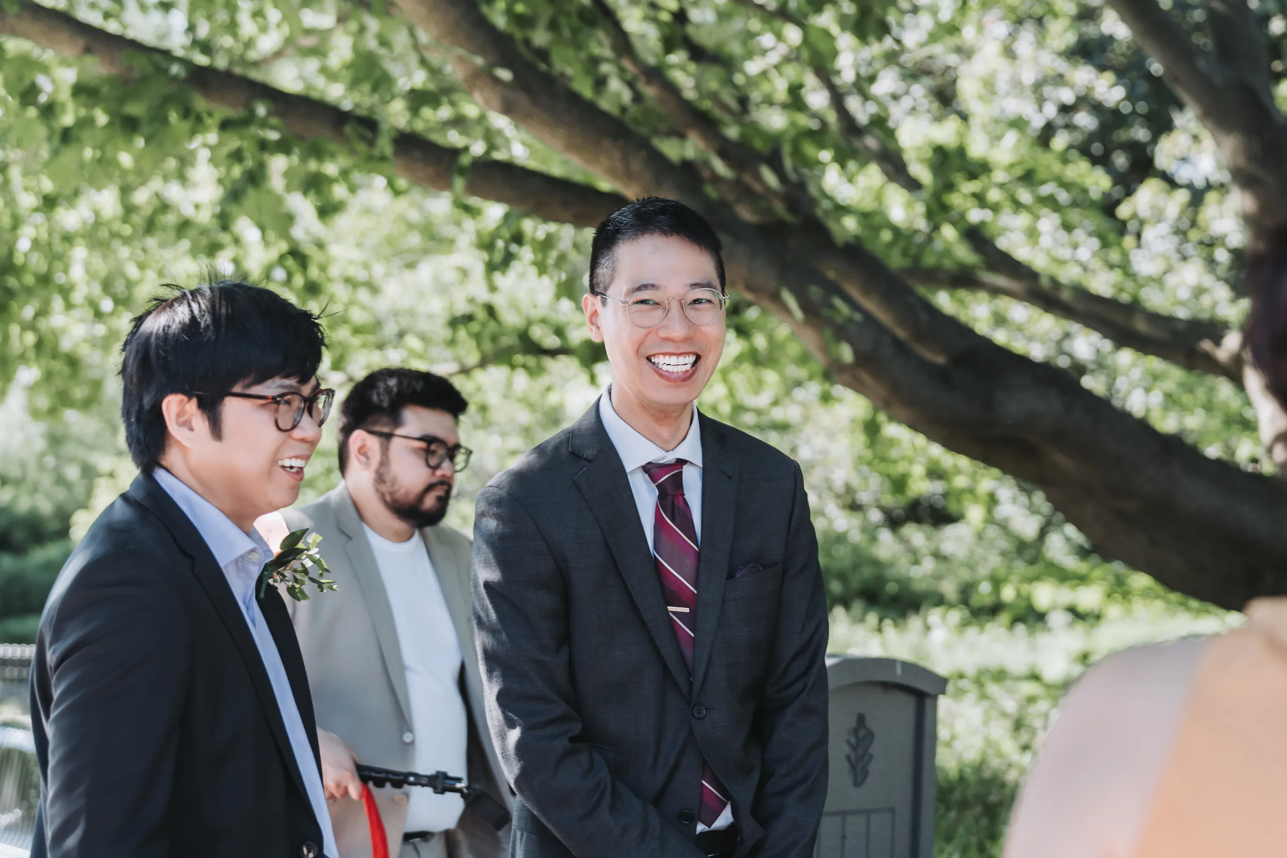 Micheal laughing with friends under the tree canopy before his Niagara Falls garden wedding, by AD Photography