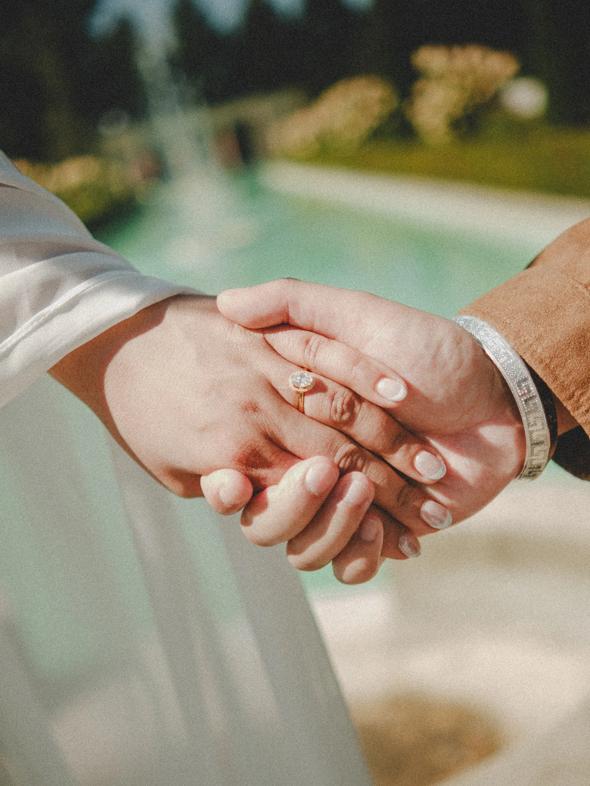 Parneet's ring and a Greek key bangle on joined hands, the turquoise pool blurred behind, by AD Photography