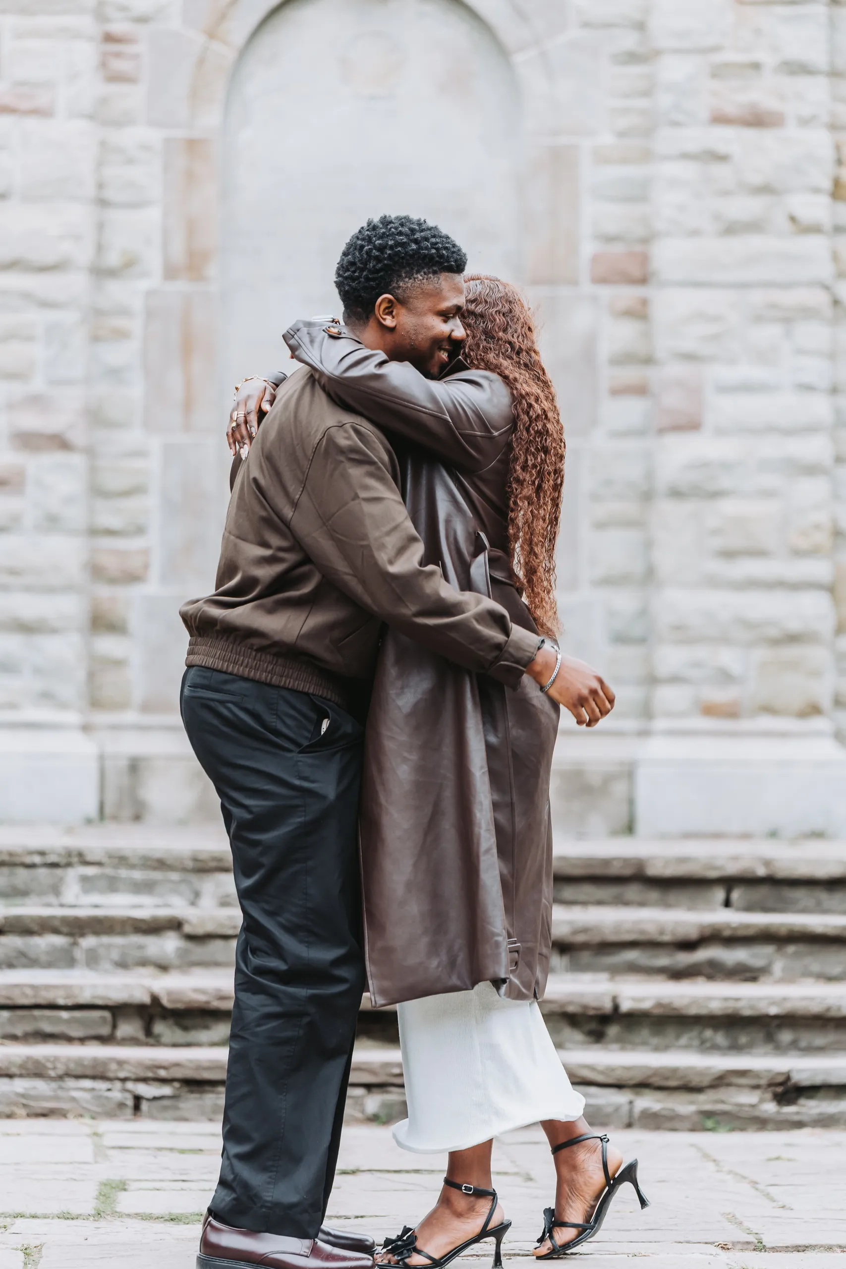Richie and Aimee in a tight hug in front of the pale stone wall right after the yes, by AD Photography