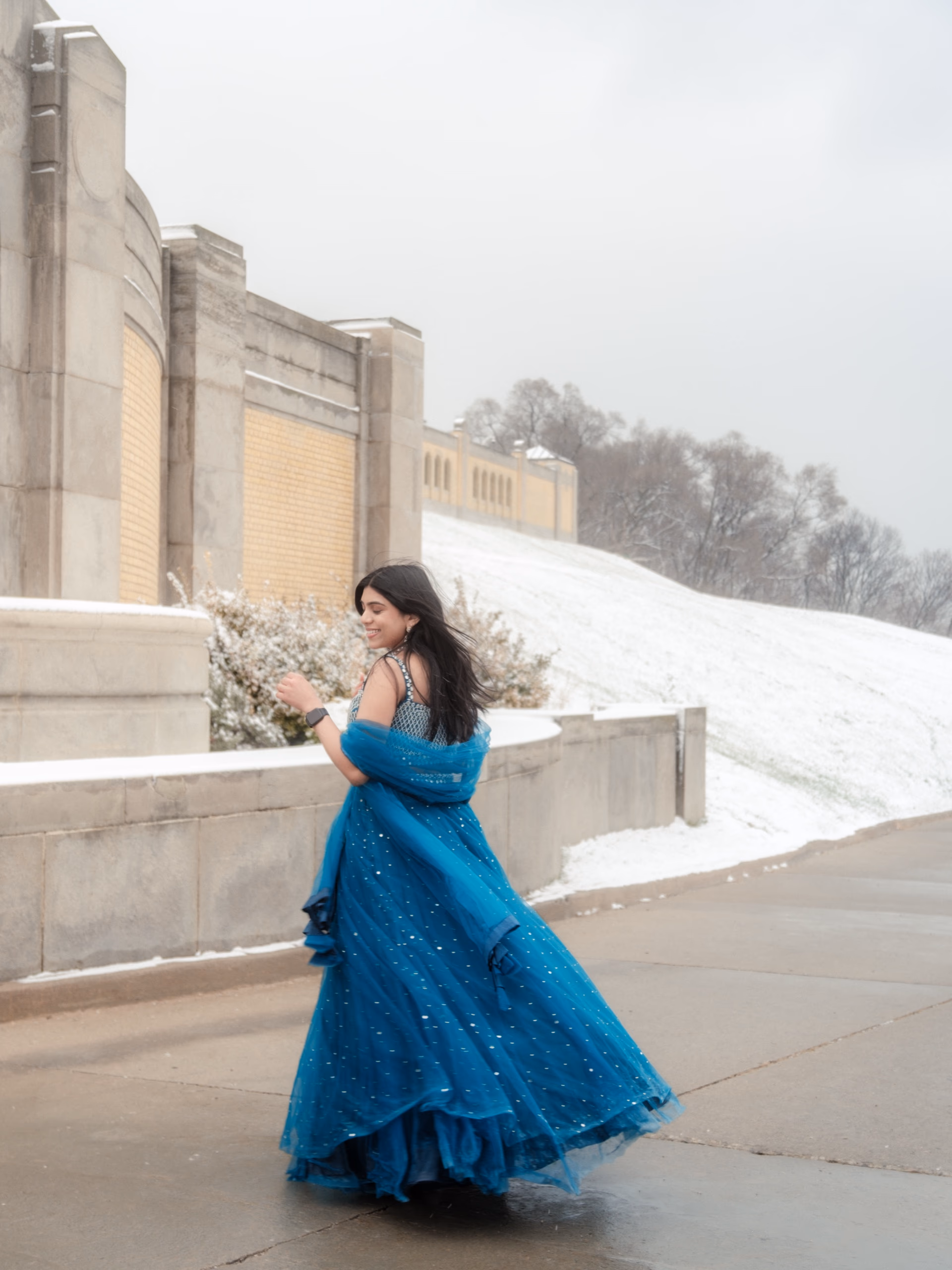 A bride to be twirls in a teal lehenga on the snowy lakeside path at RC Harris during a January engagement session in Toronto, by AD Photography