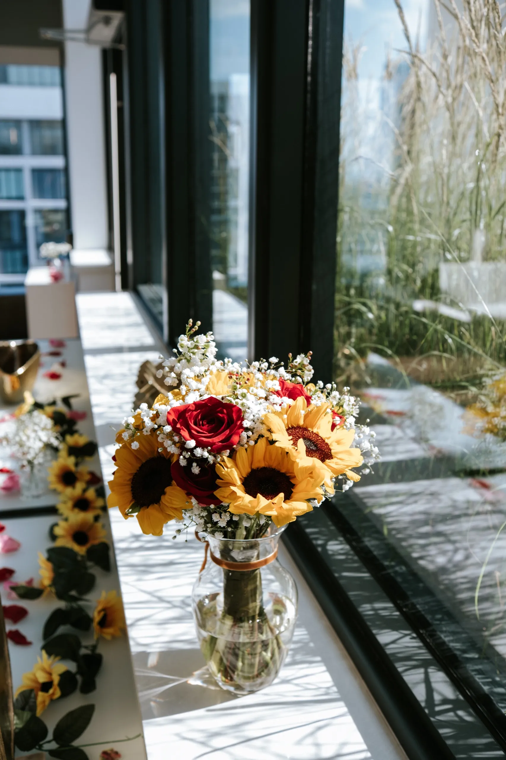 Sunflower and red rose bouquet in a glass vase on the windowsill above the terrace grasses, by AD Photography