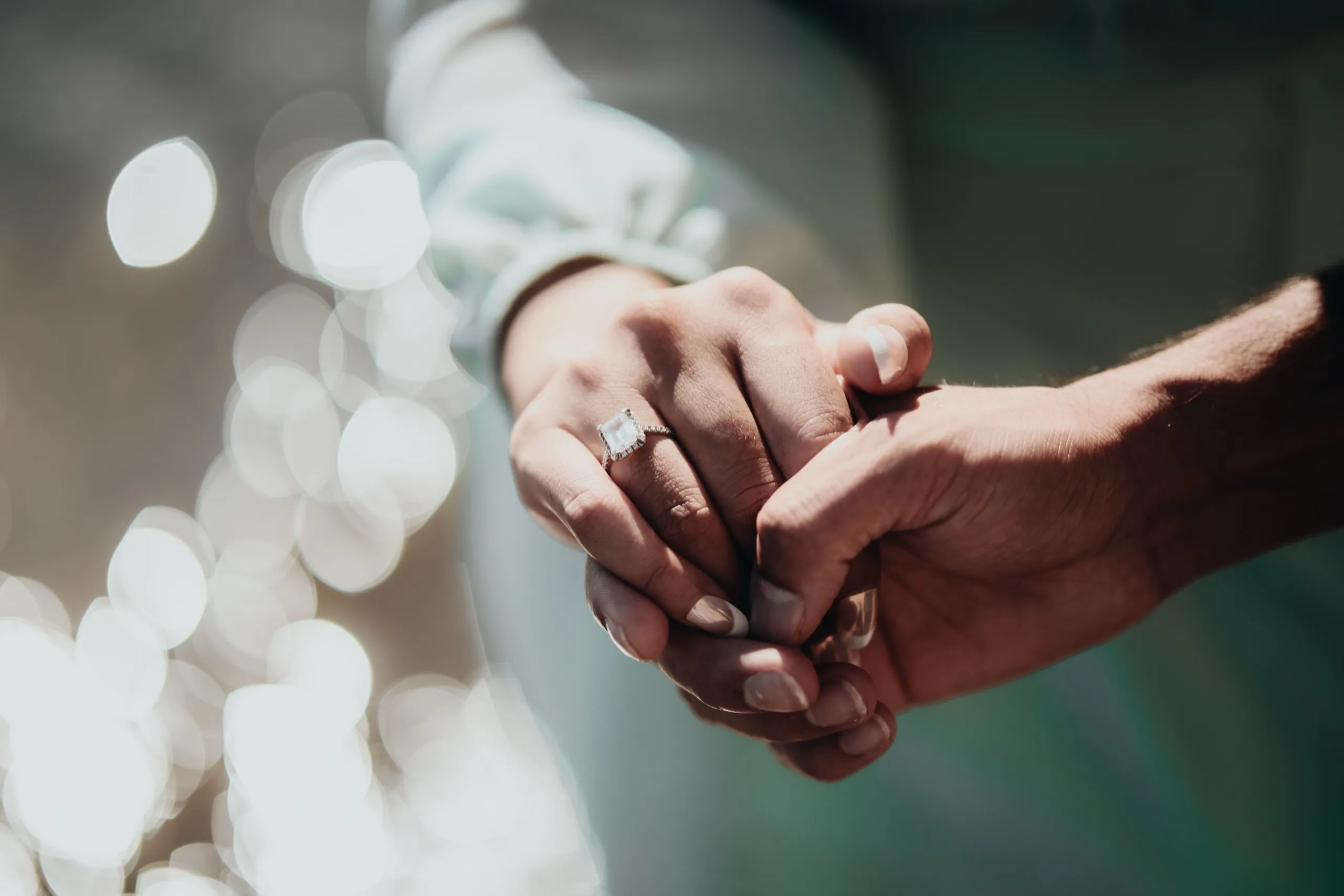 Swati's engagement ring sparkles in clasped hands against glittering water bokeh at the Bluffs, by AD Photography