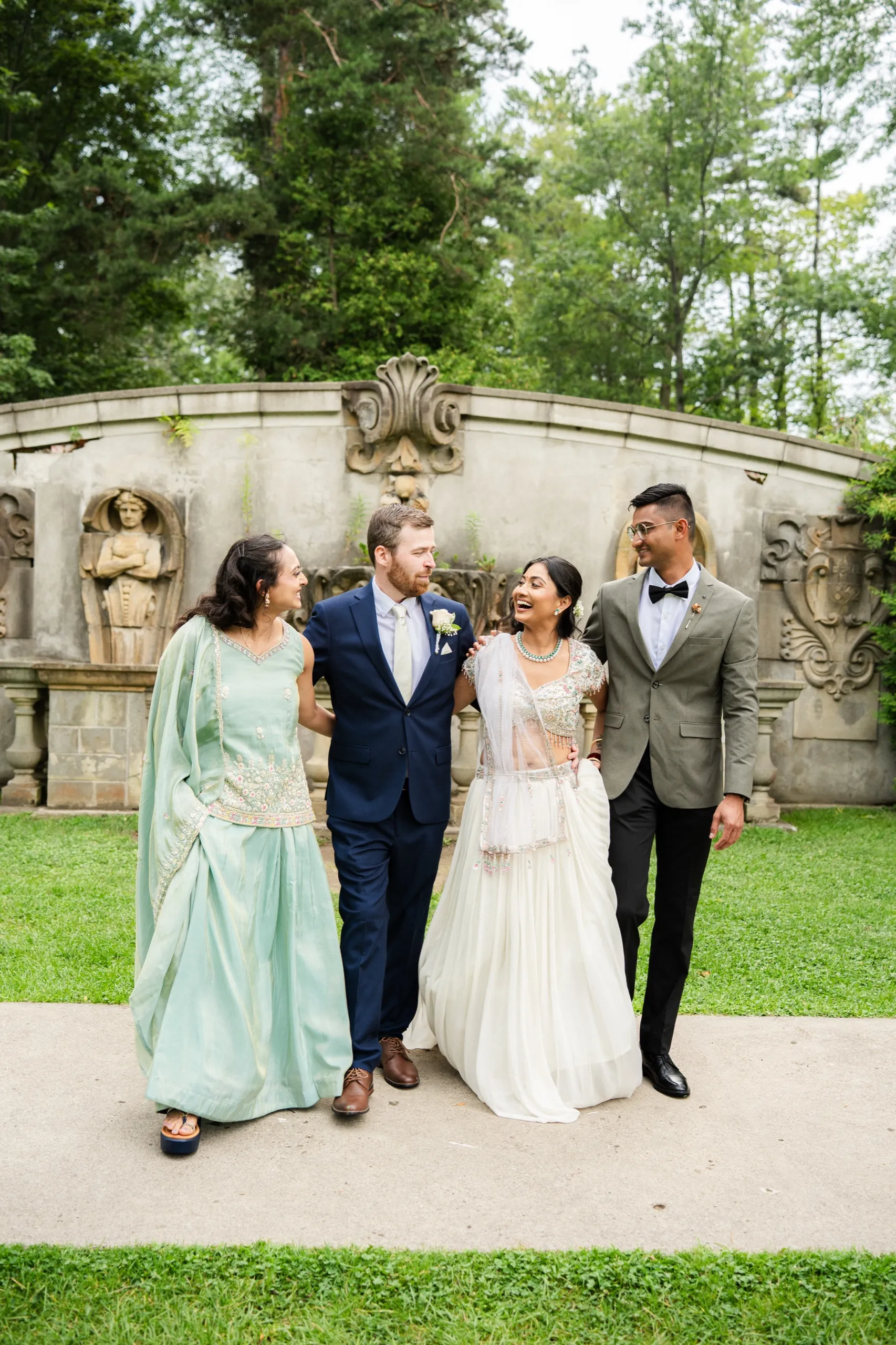 Nidhi and Derek walk laughing with two guests past a carved stone fountain., by AD Photography
