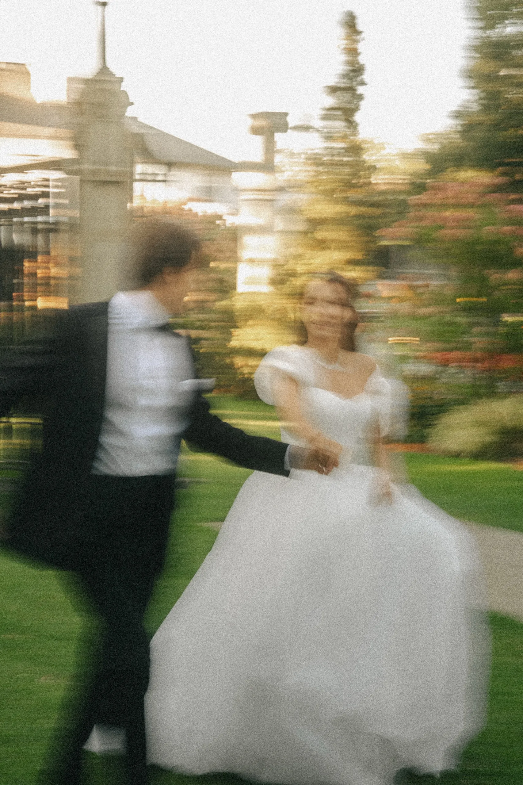 Motion blur as the groom pulls the bride across the lawn by the hand at sunset, by AD Photography