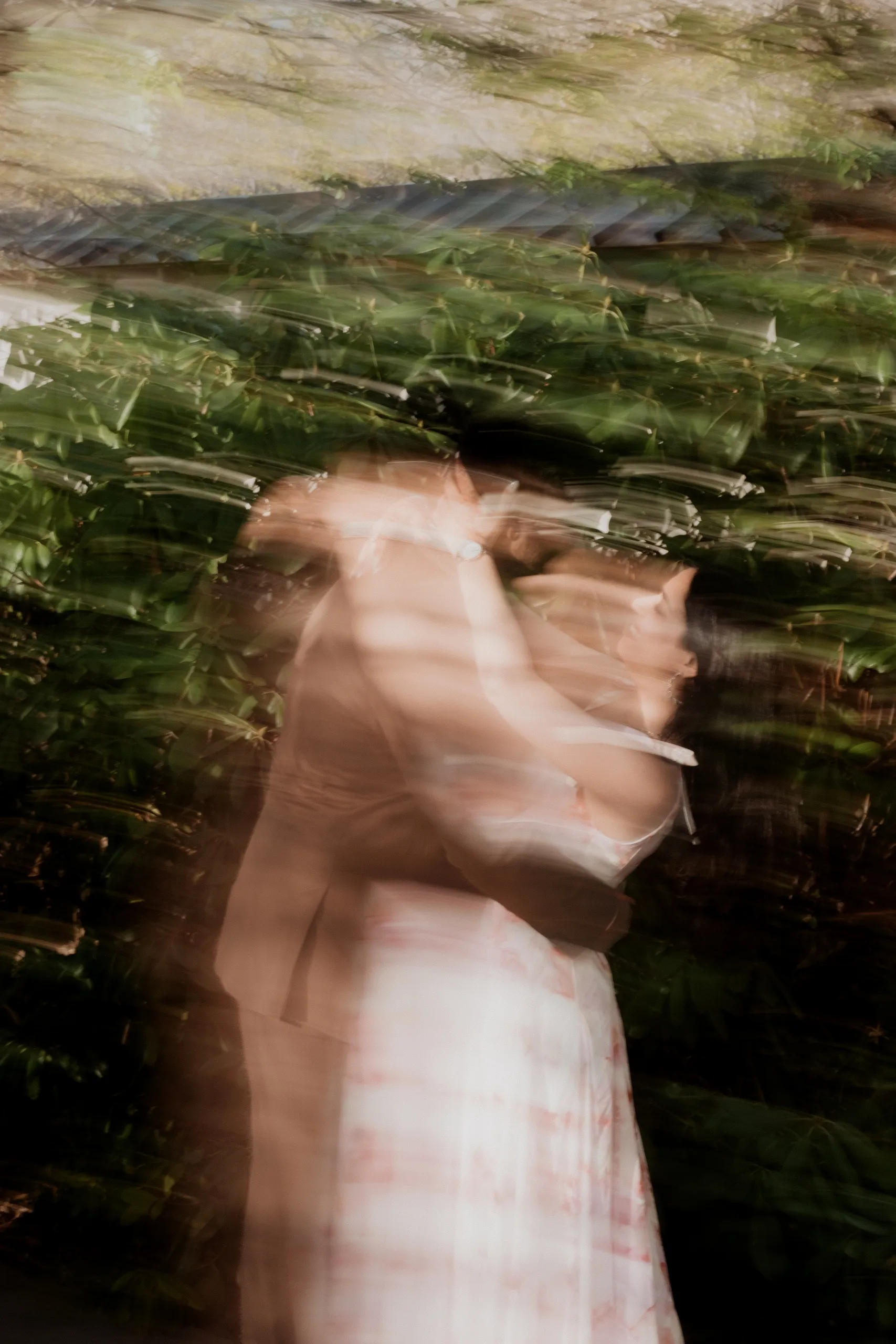 Soft motion blur of Mehak and Kamal wrapped together against a garden hedge, by AD Photography
