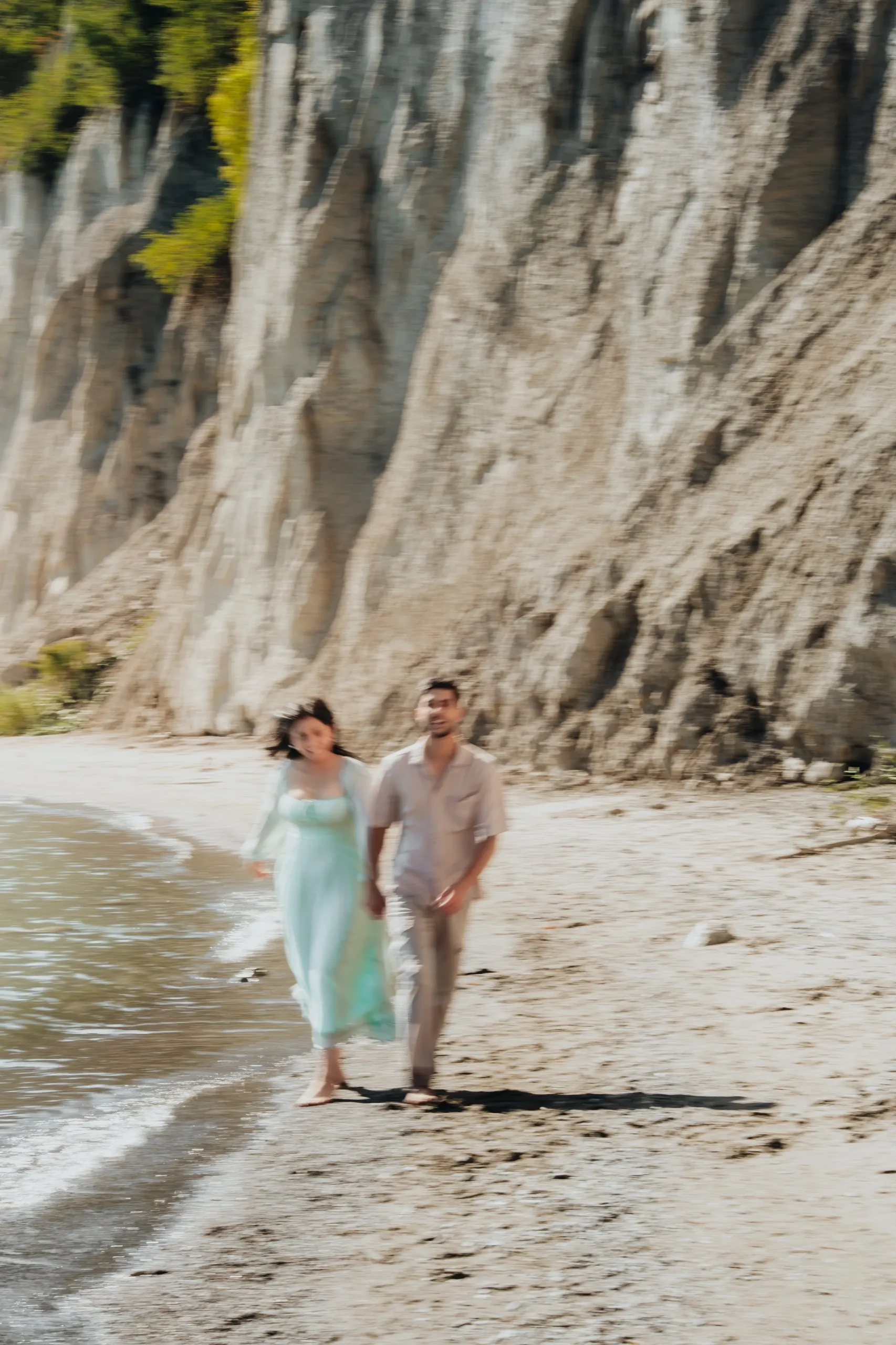Soft motion blur of a couple walking the sand hand in hand beneath the Scarborough Bluffs, by AD Photography