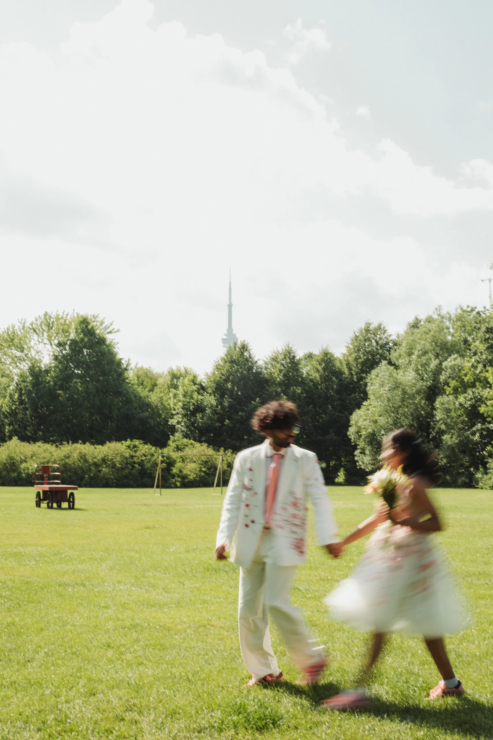 Harsh and Payal running through a Toronto Islands field, motion blurred, CN Tower on the horizon, by AD Photography