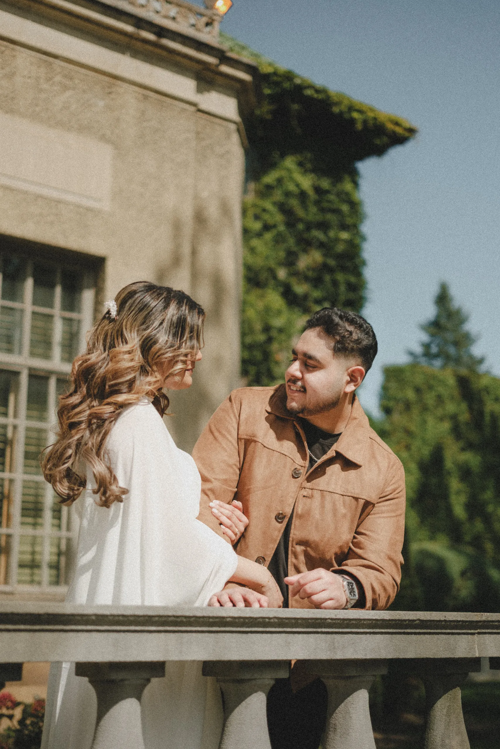 Leaning on a stone balustrade, Maninder laughs while Parneet holds his arm and watches him, by AD Photography