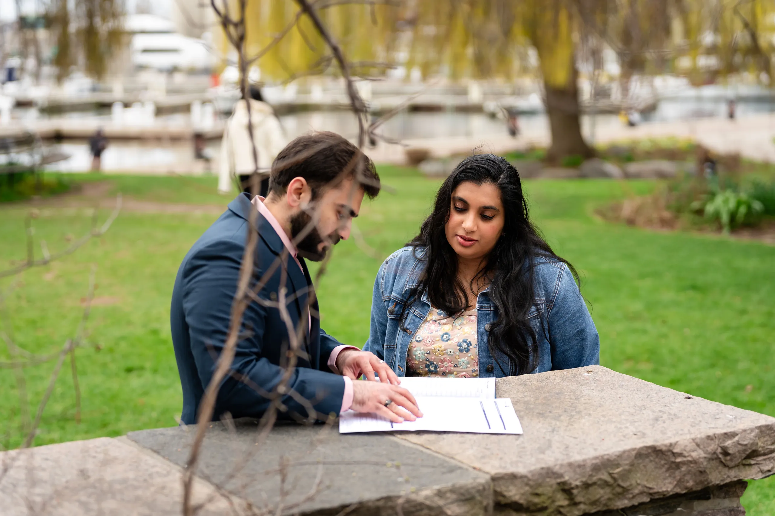 Abdullah and Nadia read their marriage documents at a stone table framed by bare spring branches, by AD Photography