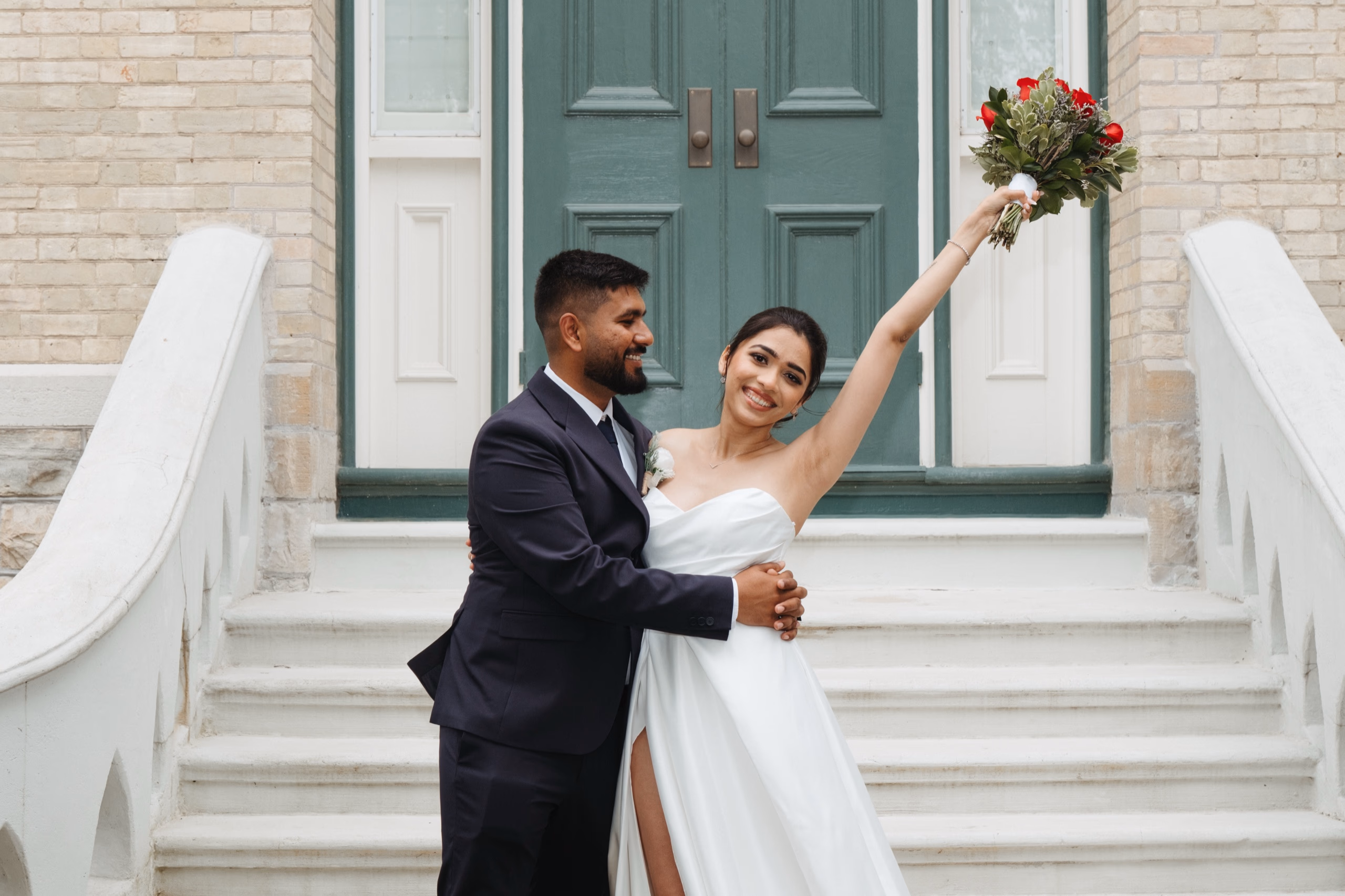 Purv embraces Mitali as she lifts her bouquet outside the green doors at Kawartha