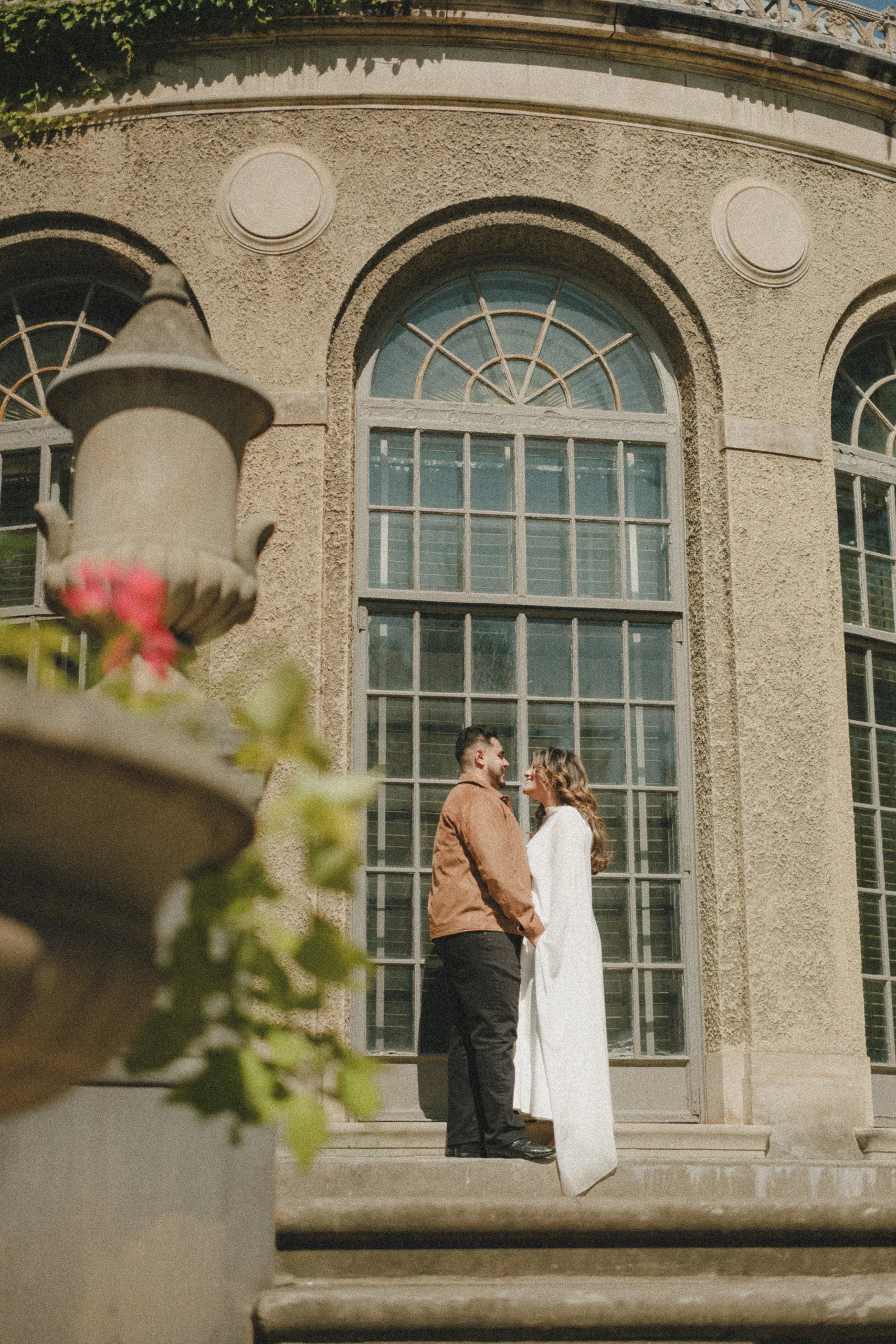 Maninder and Parneet on the stone steps under a tall arched window of the Parkwood mansion, seen past a stone urn, by AD Photography