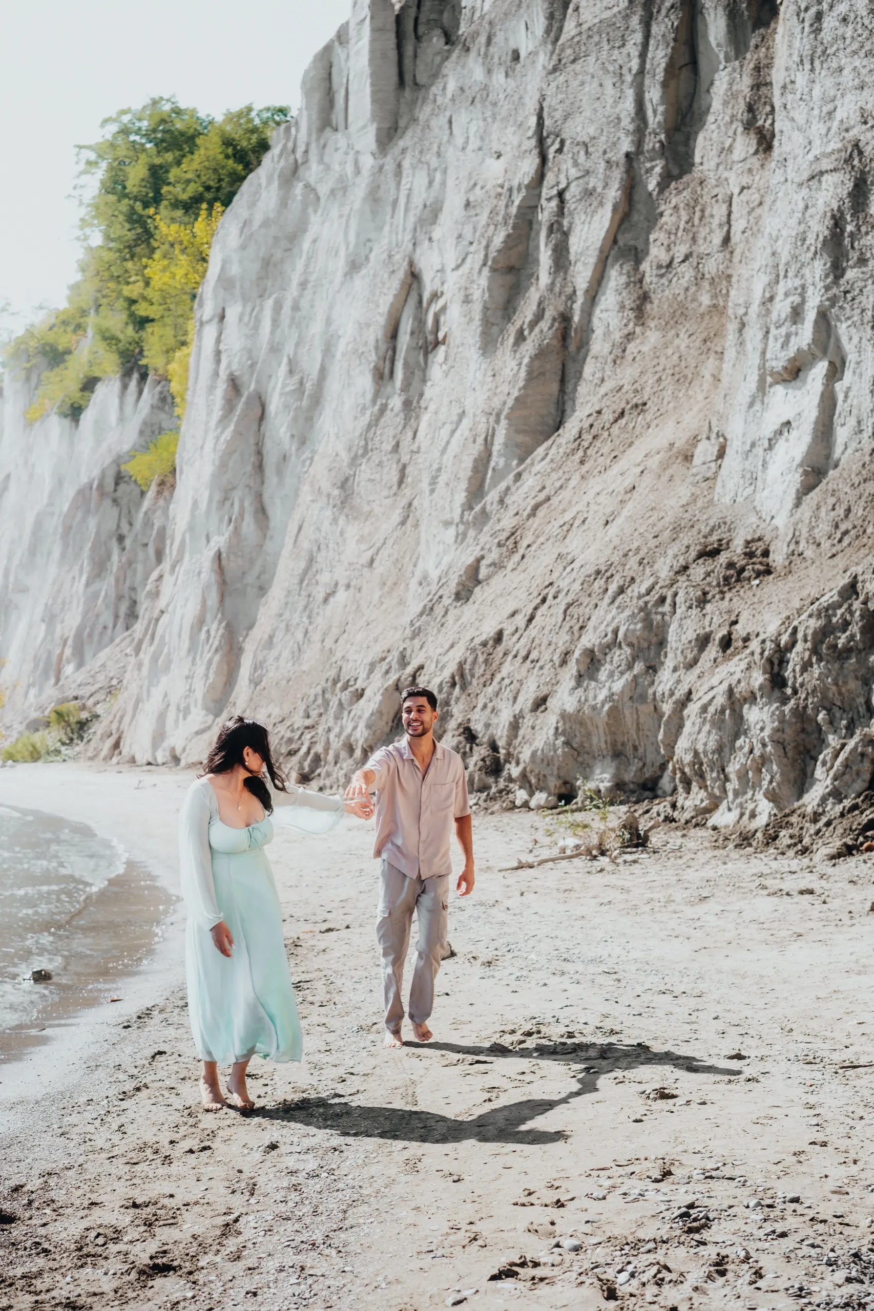 Linked hands mid chase as the couple laughs along the white cliff shoreline, by AD Photography