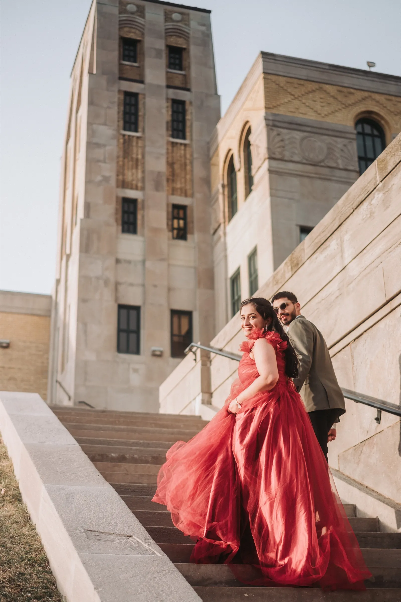 Red gown cascading down the art deco staircase at golden hour, editorial pre-wedding frame, by AD Photography