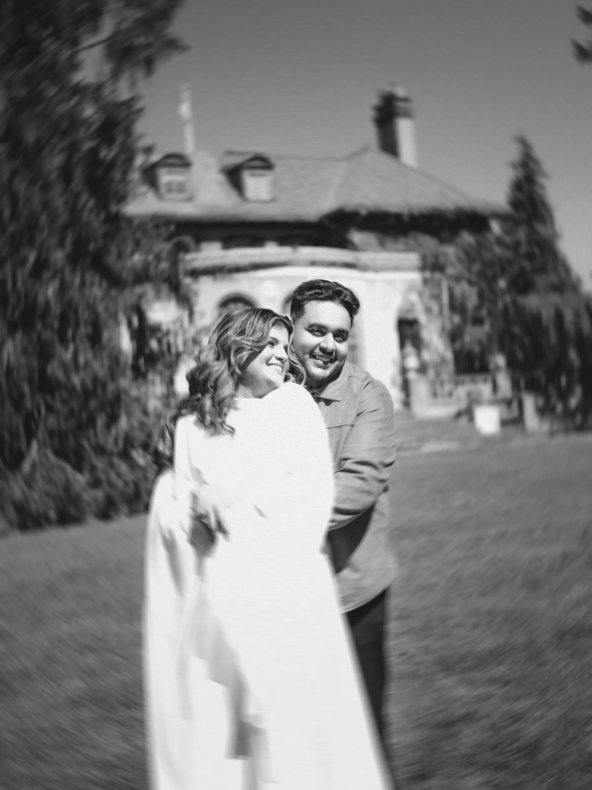 Soft edged black and white of Maninder wrapping Parneet in a laughing hug before the Parkwood mansion, by AD Photography