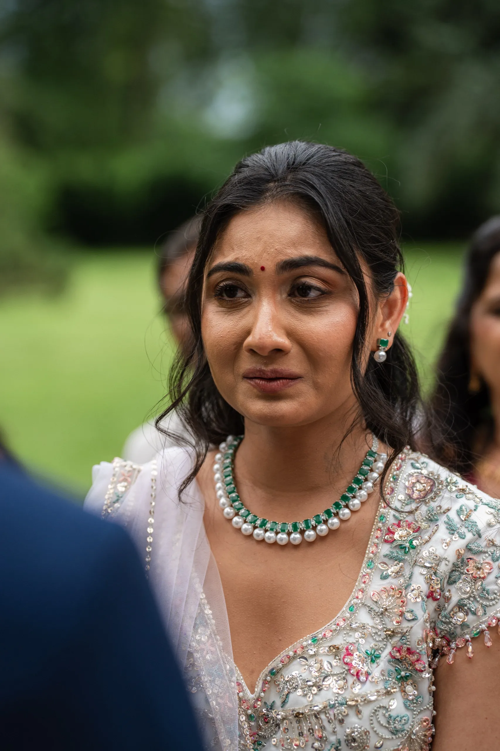 Nidhi's eyes glisten during her vows, bindi and emerald pearls bright against her lehenga., by AD Photography