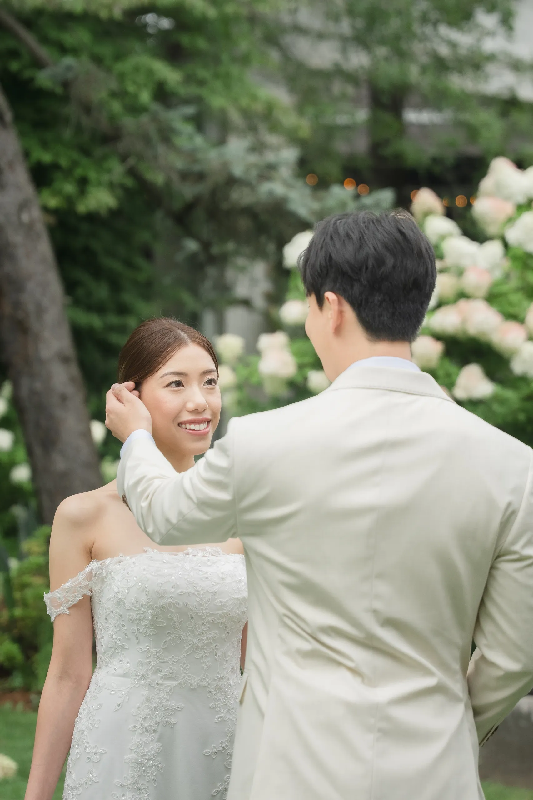 Nelson tucking a loose strand behind Josie's ear beside the hydrangea wall, by AD Photography