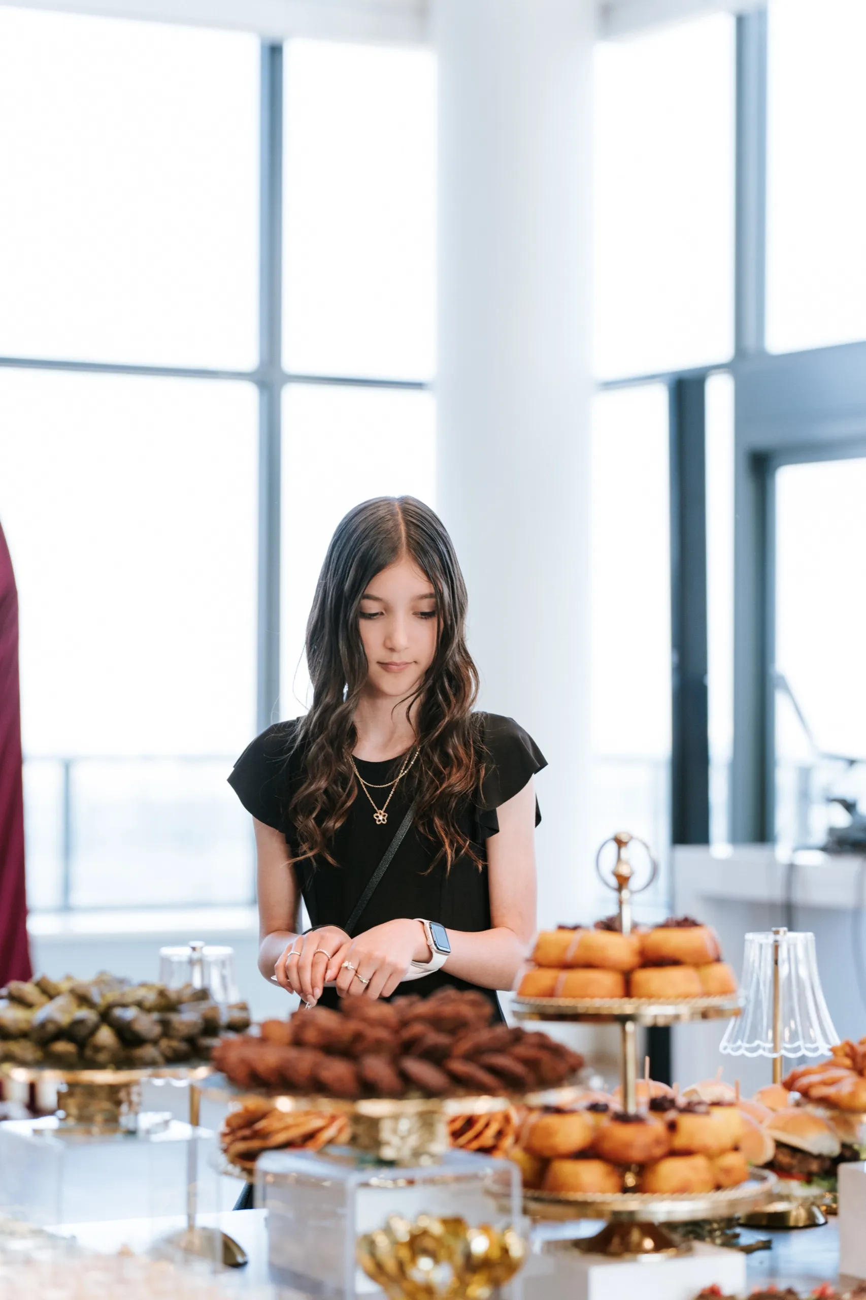A young guest chooses from the dessert table of donuts and bundt cakes by the windows, by AD Photography