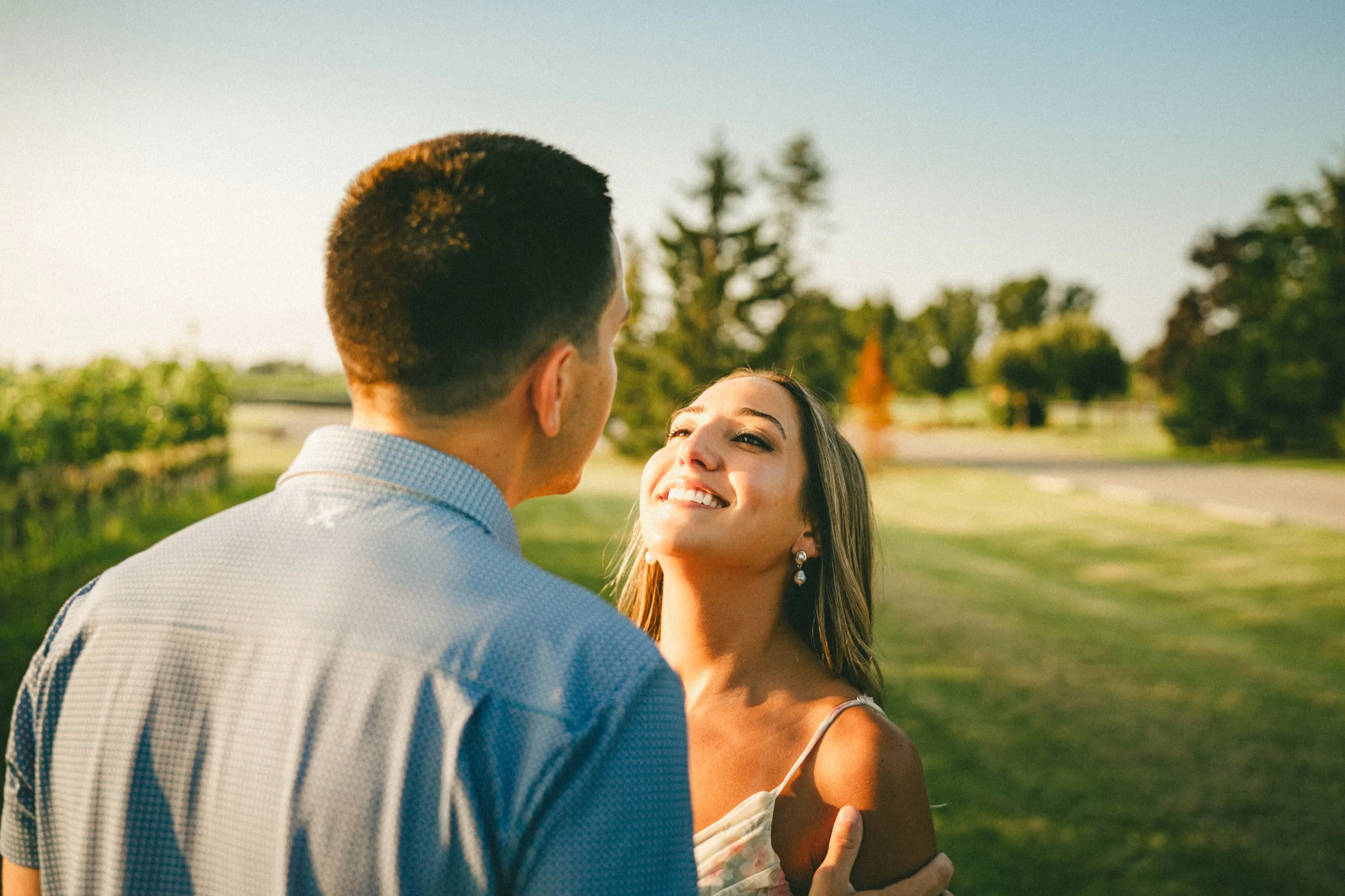 Ashley looking up at Donald and laughing, rim lit by the last of the gold light on the winery lawn, by AD Photography