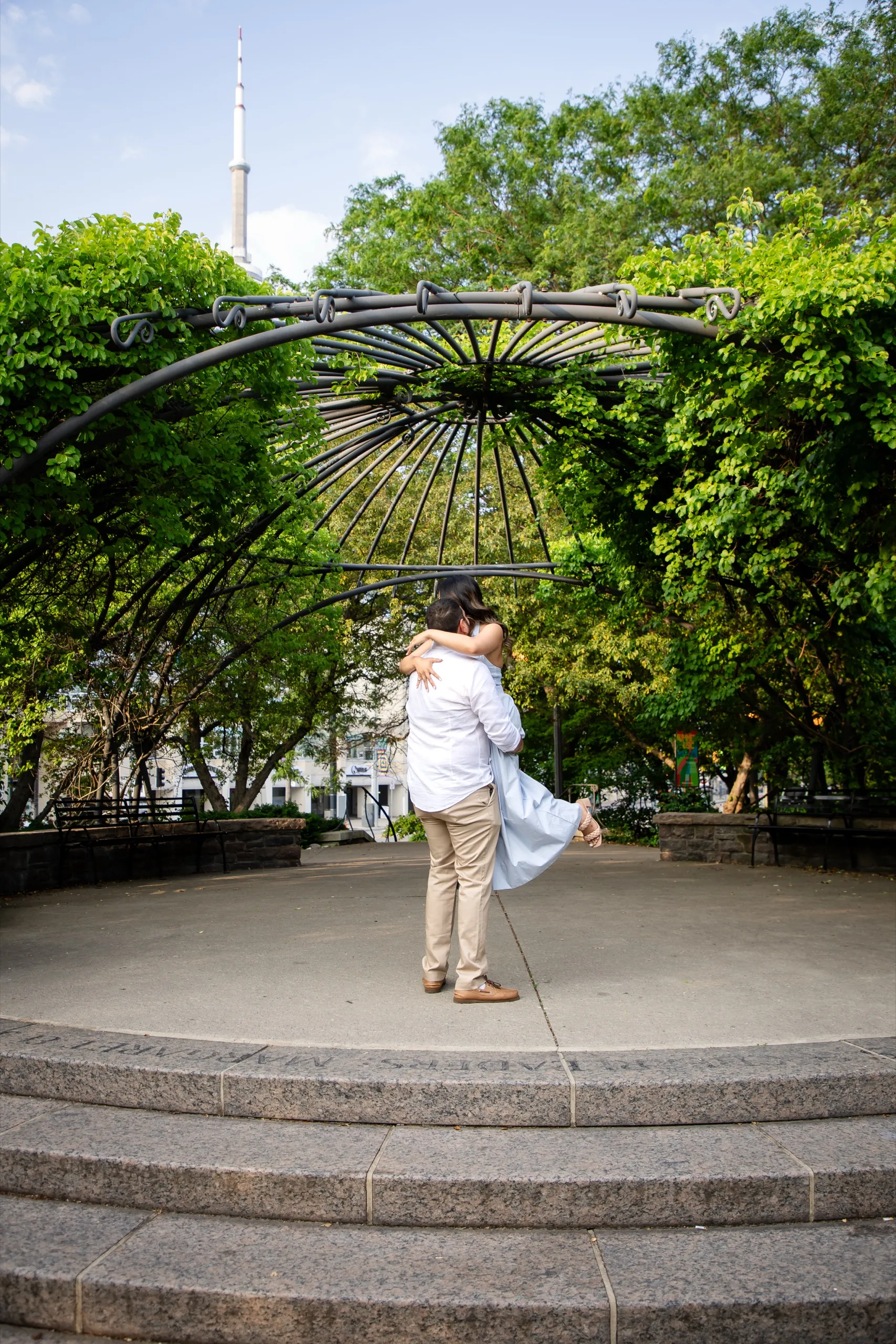Mike lifting Margarita off the ground at the Toronto Music Garden with the CN Tower in the background, by AD Photography